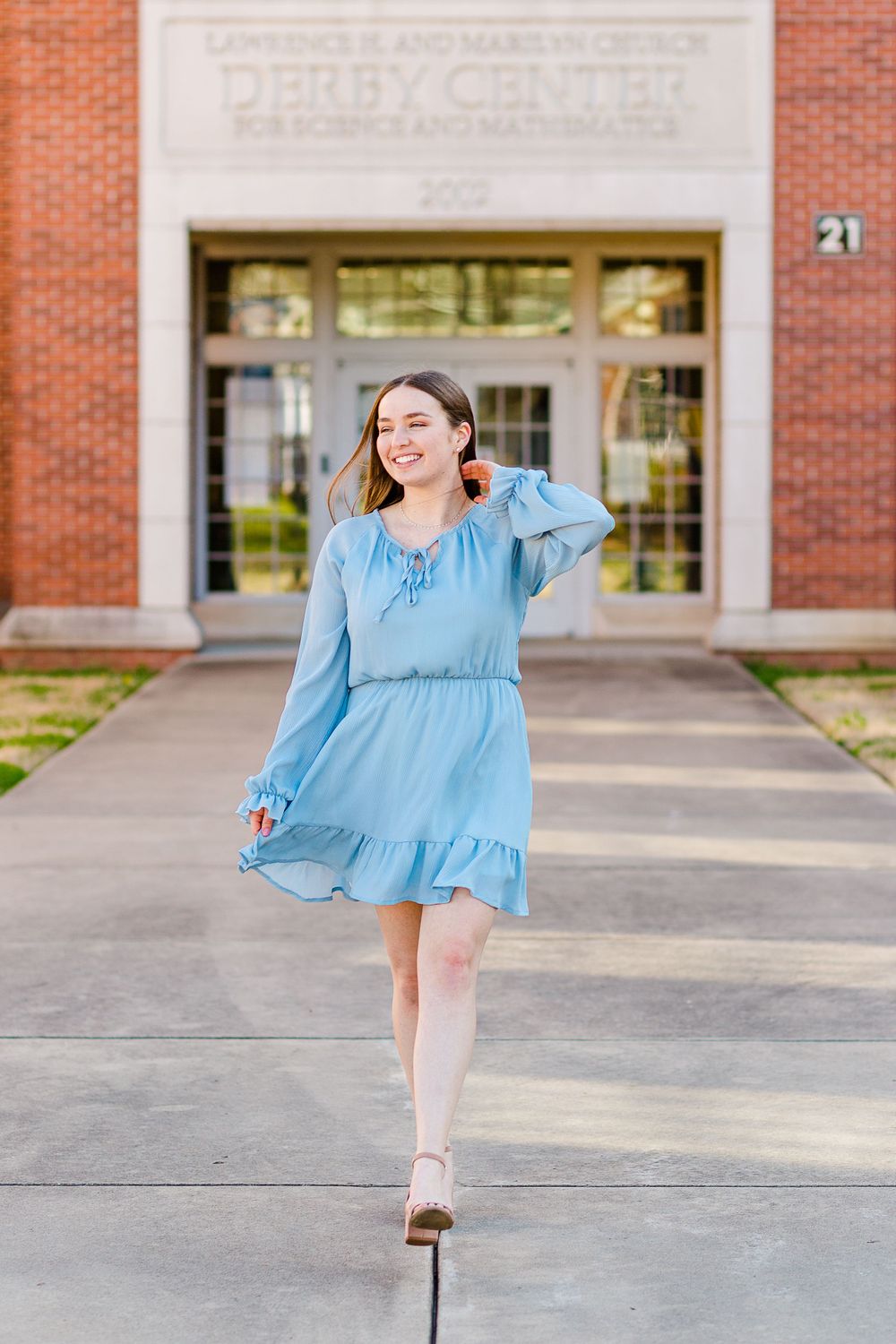A flowing light blue dress moves gracefully in front of a brick academic building entrance.
