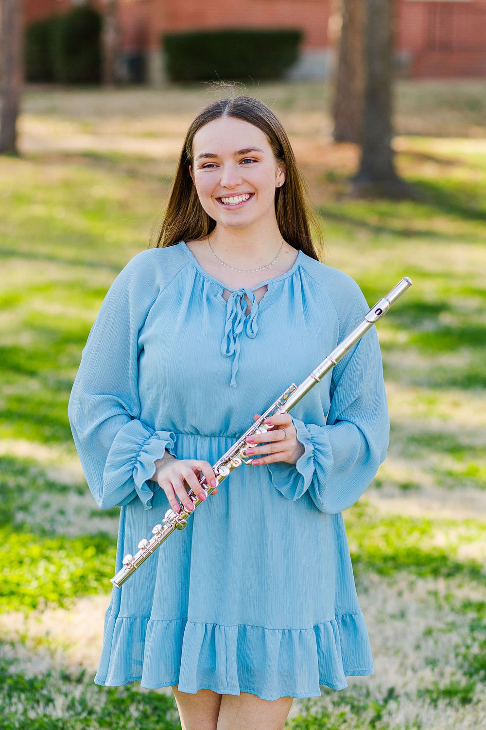 A silver flute is held against a light blue dress on a sunny spring day.