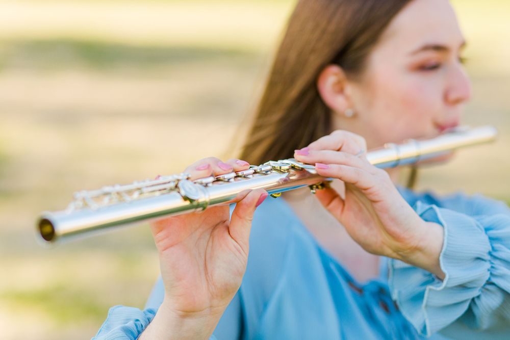 Close-up of hands playing a silver flute with blue sleeves visible.