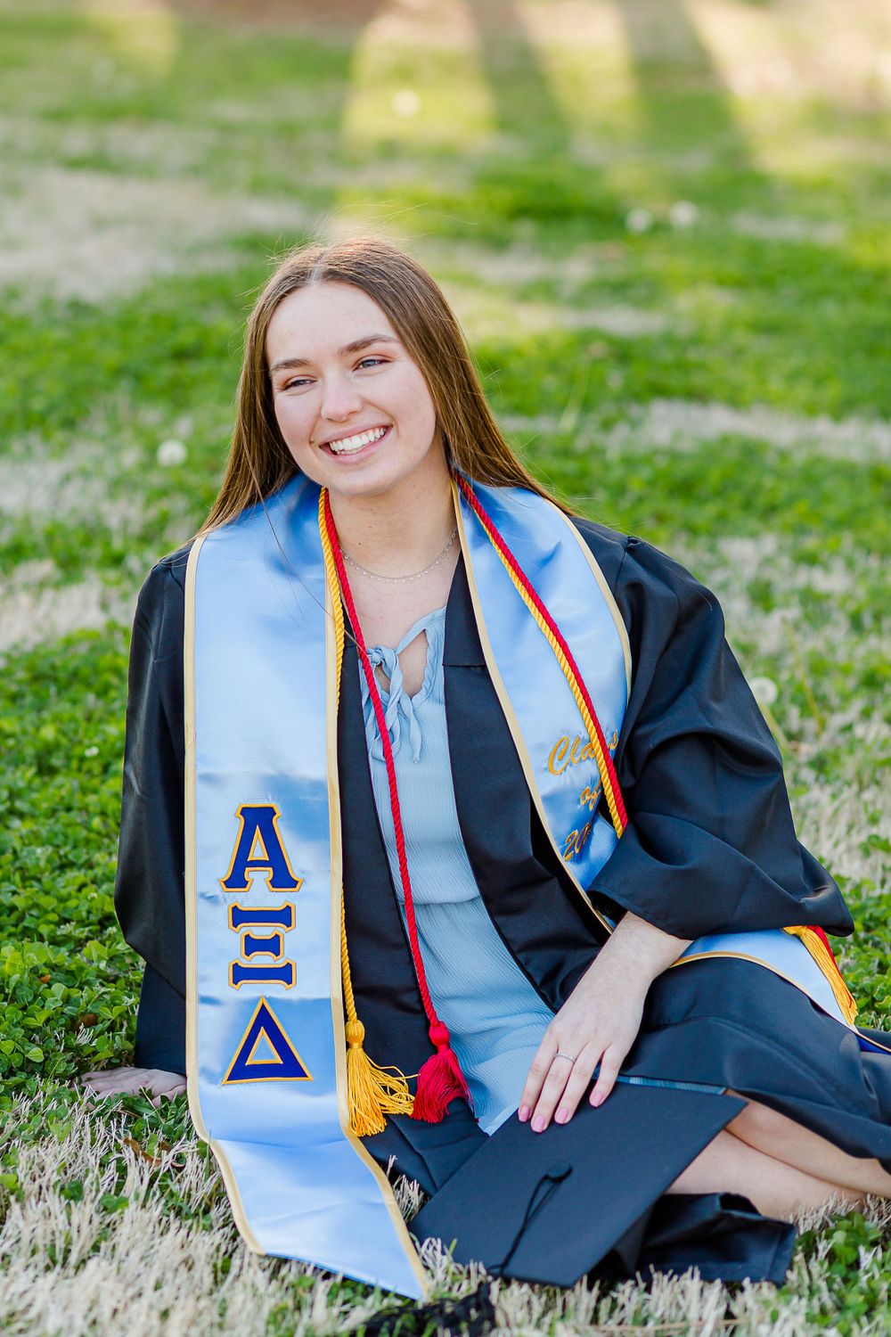 Graduate wearing Alpha Xi Delta stole poses sitting on grass during spring graduation photos.