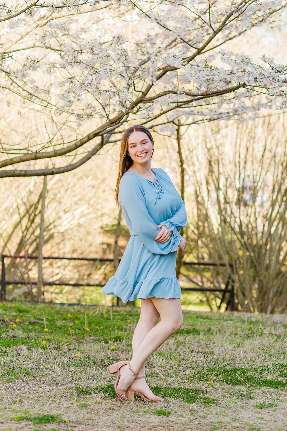 A springtime portrait under blooming cherry blossoms with a blue dress and sandals.