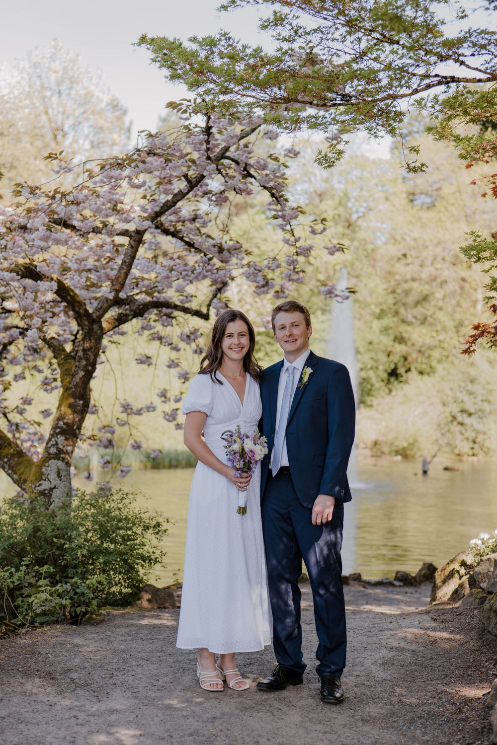 Bride and groom standing arm in arm under blooming cherry tree