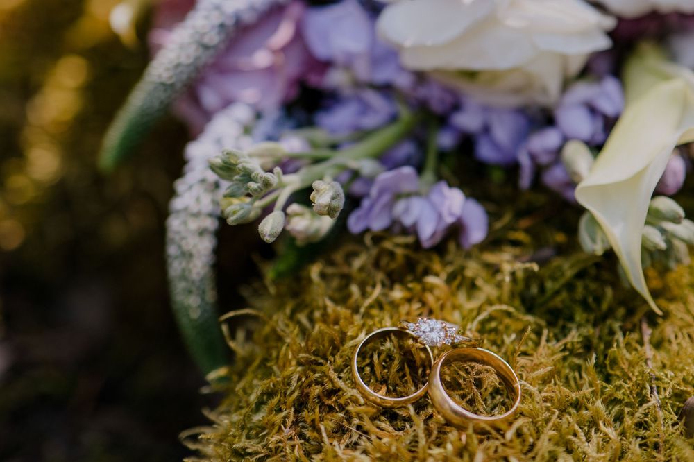 Wedding ring and band resting on mossy log with flowers