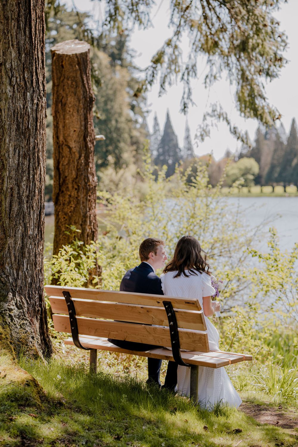 Bride and groom quietly sitting on wooden bench together looking over a river