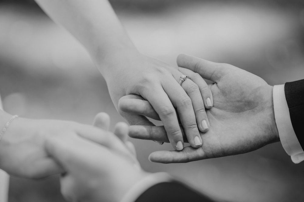 Close up of bride and groom holding hands with wedding ring showing
