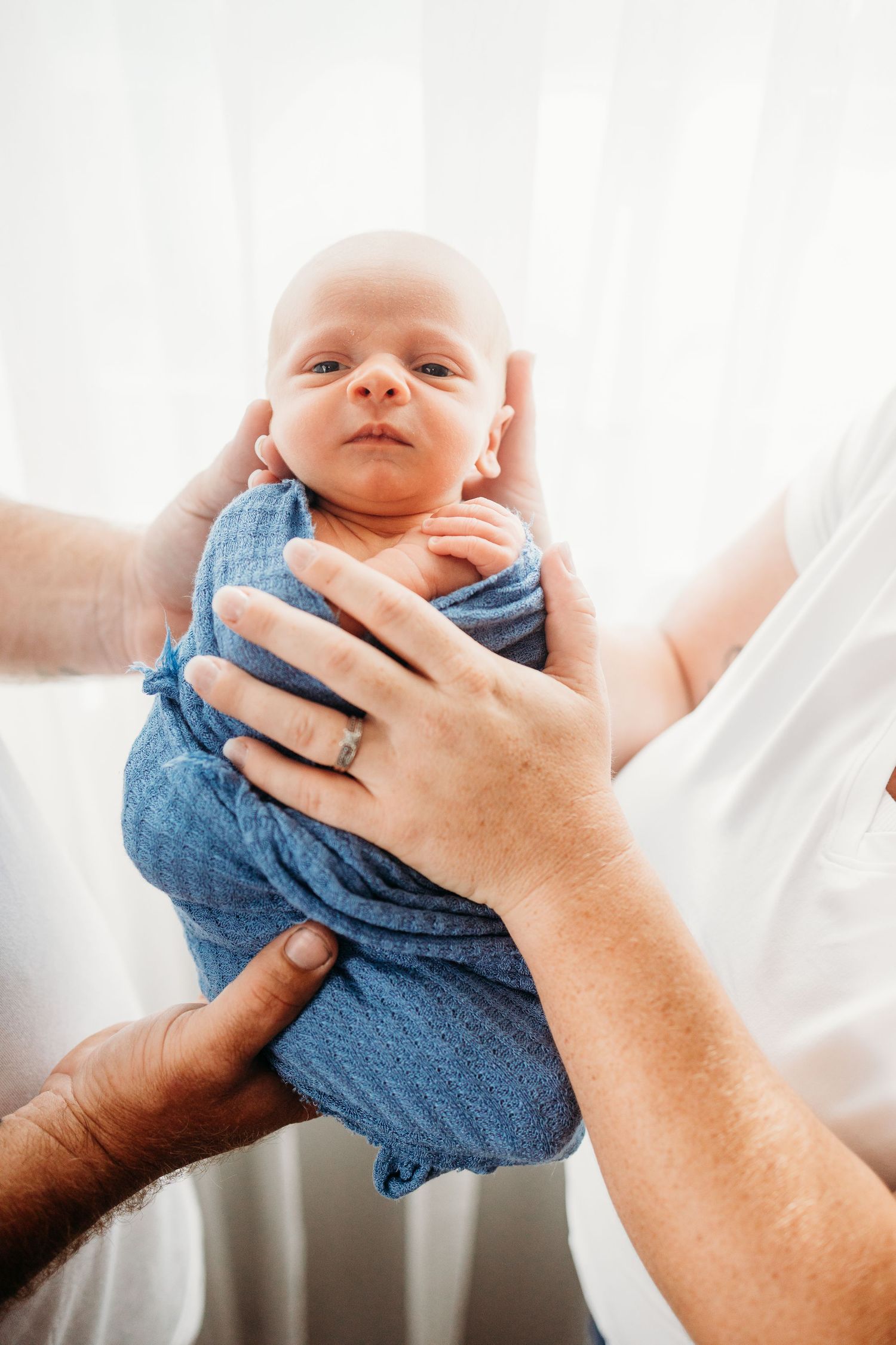 Baby wrapped in blue fabric held gently against white background.