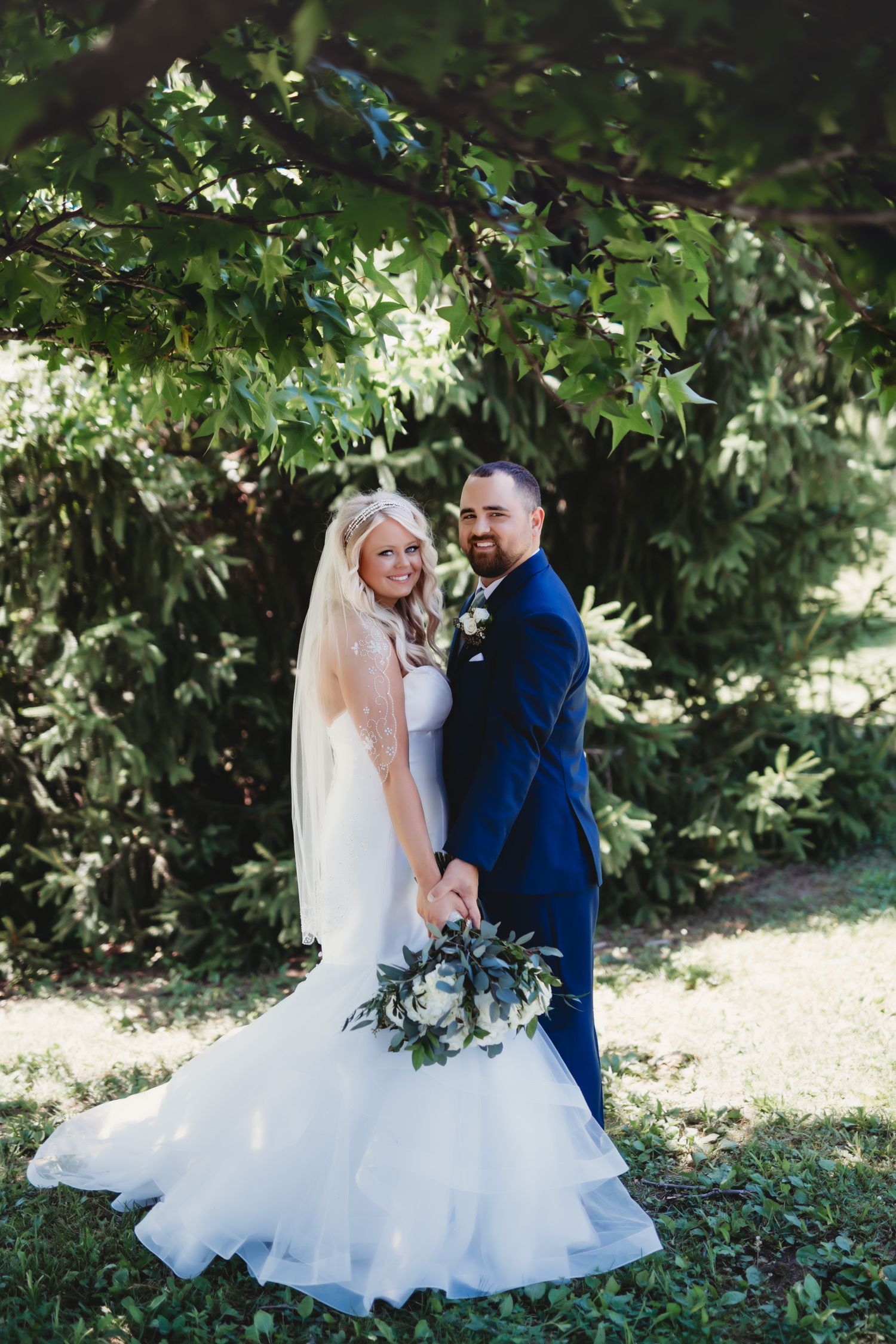 Newlyweds share a tender moment in garden setting with lush greenery.