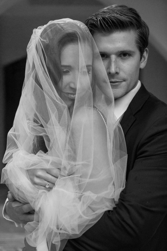 A groom hugs his bride while she is wrapped under her veil on a rainy day at Toadbury Hall.