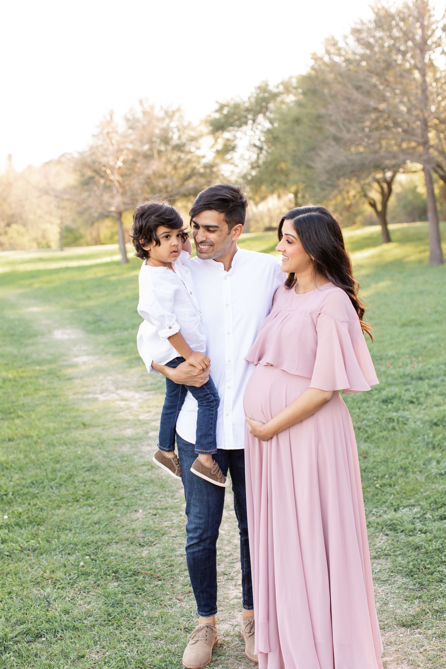 A sunny outdoor family portrait with a woman in pink dress and natural park scenery.