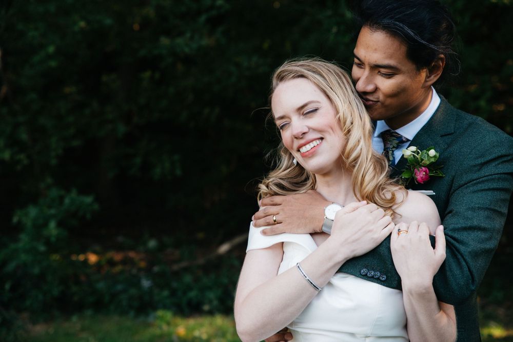 A tender embrace between newlyweds outdoors with greenery in the background.