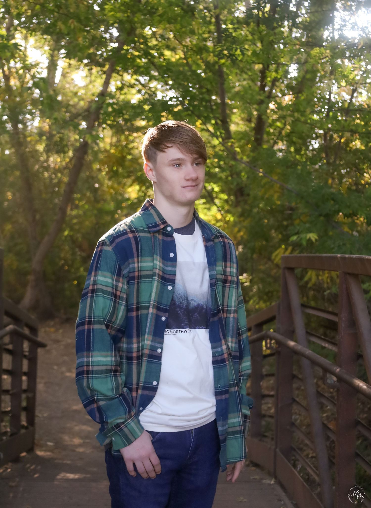 Portrait on wooden bridge with plaid shirt and sunlit forest background.