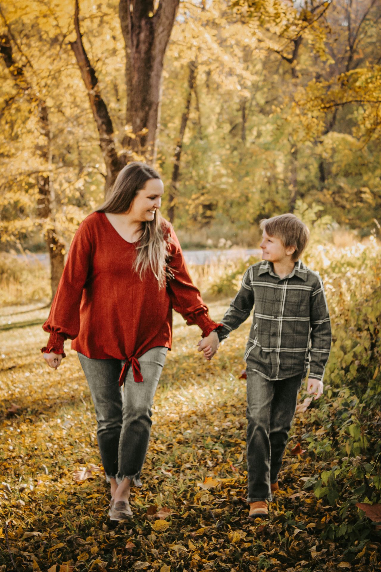 Two people walk hand in hand along an autumn path lined with golden trees.