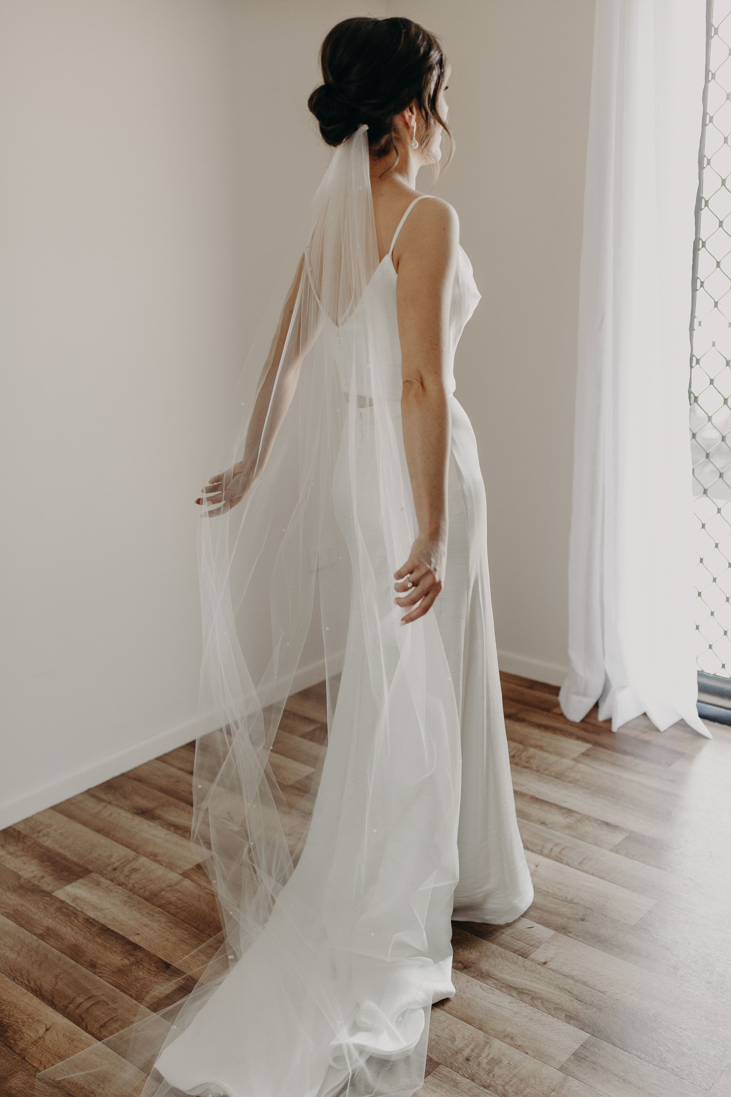 Elegant white wedding dress with flowing veil captured in natural light.