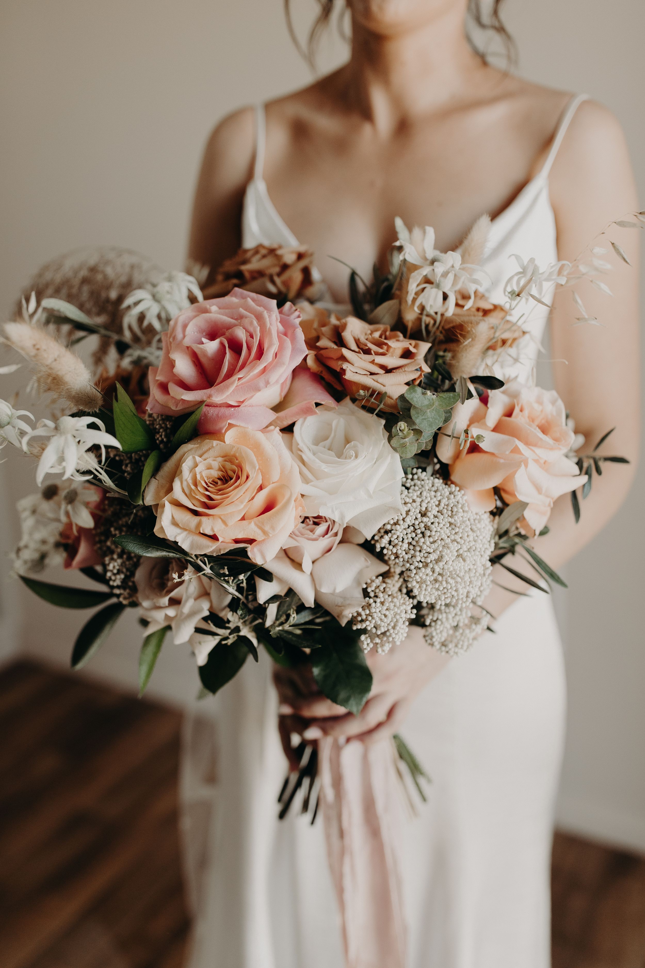 Elegant blush pink and white wedding bouquet with roses and delicate greenery held against a white dress.