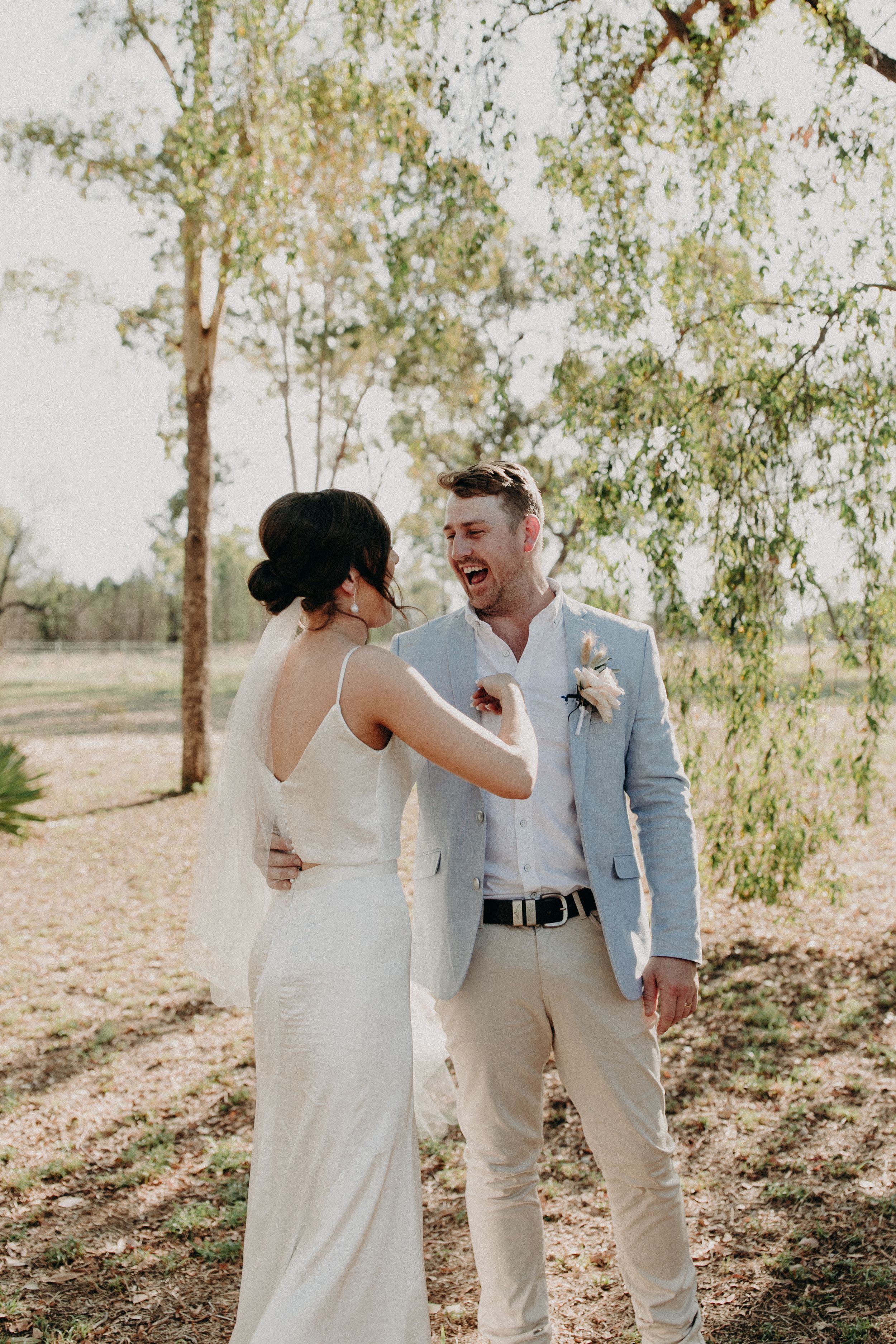 Wedding couple sharing intimate moments under trees in light colored attire.