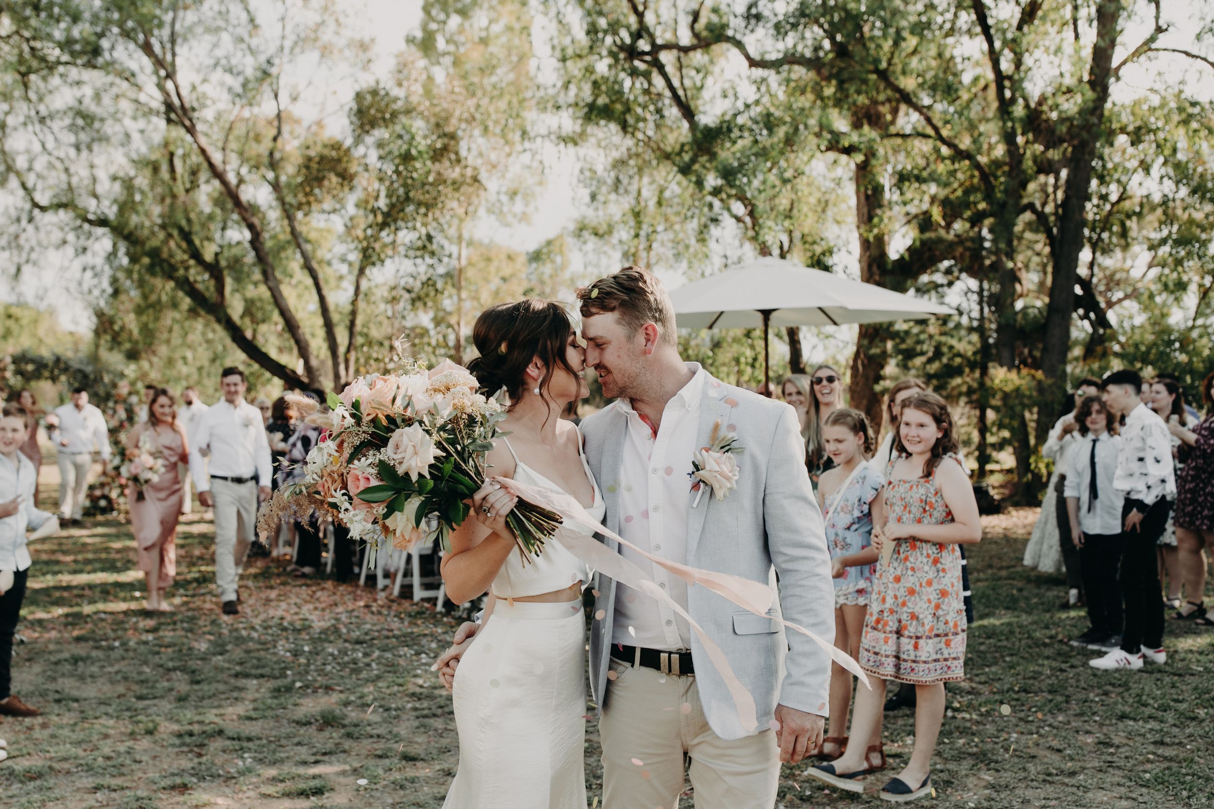 Wedding party and guests gather for celebration in natural outdoor setting.