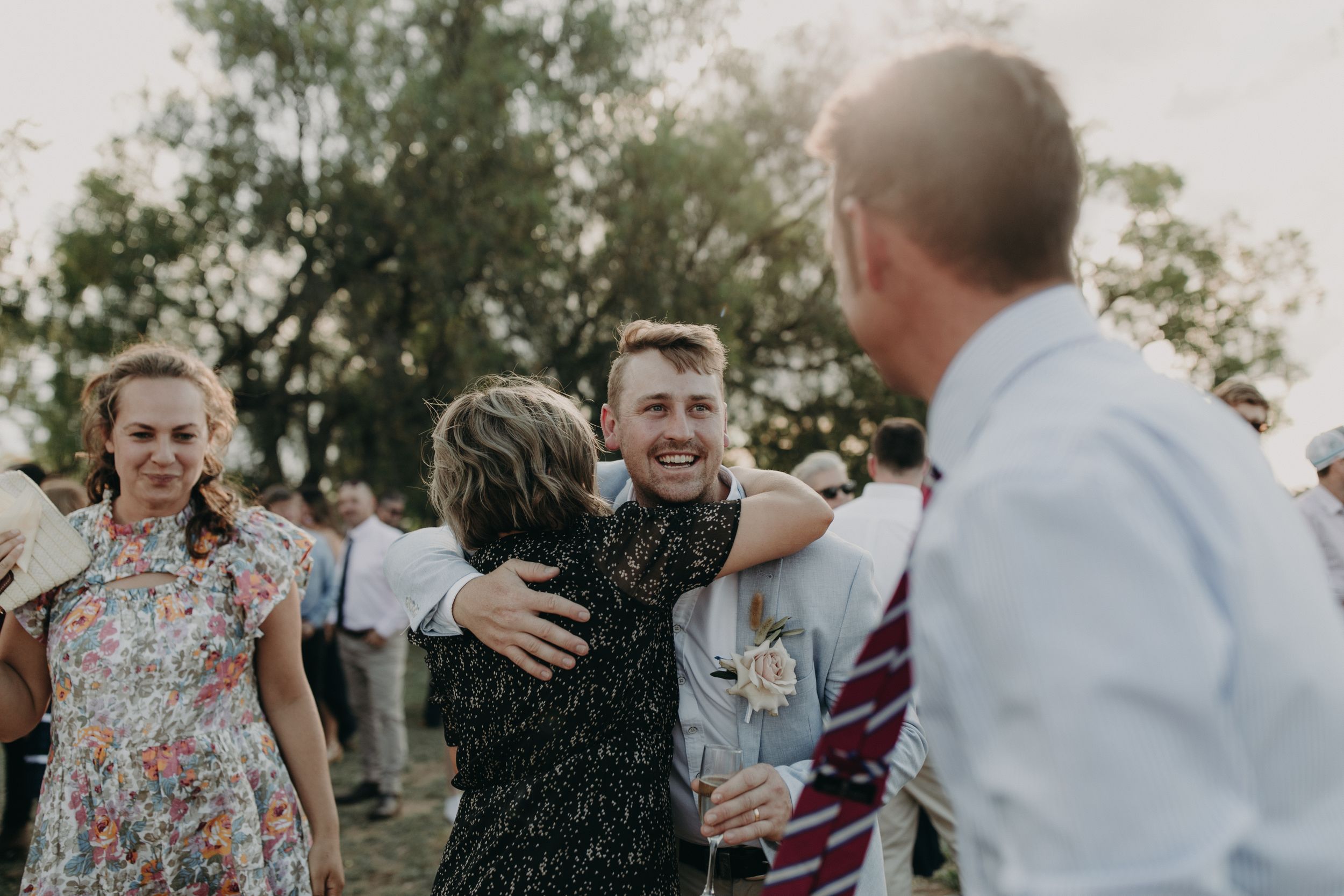Wedding celebration with guests mingling outdoors in natural lighting.