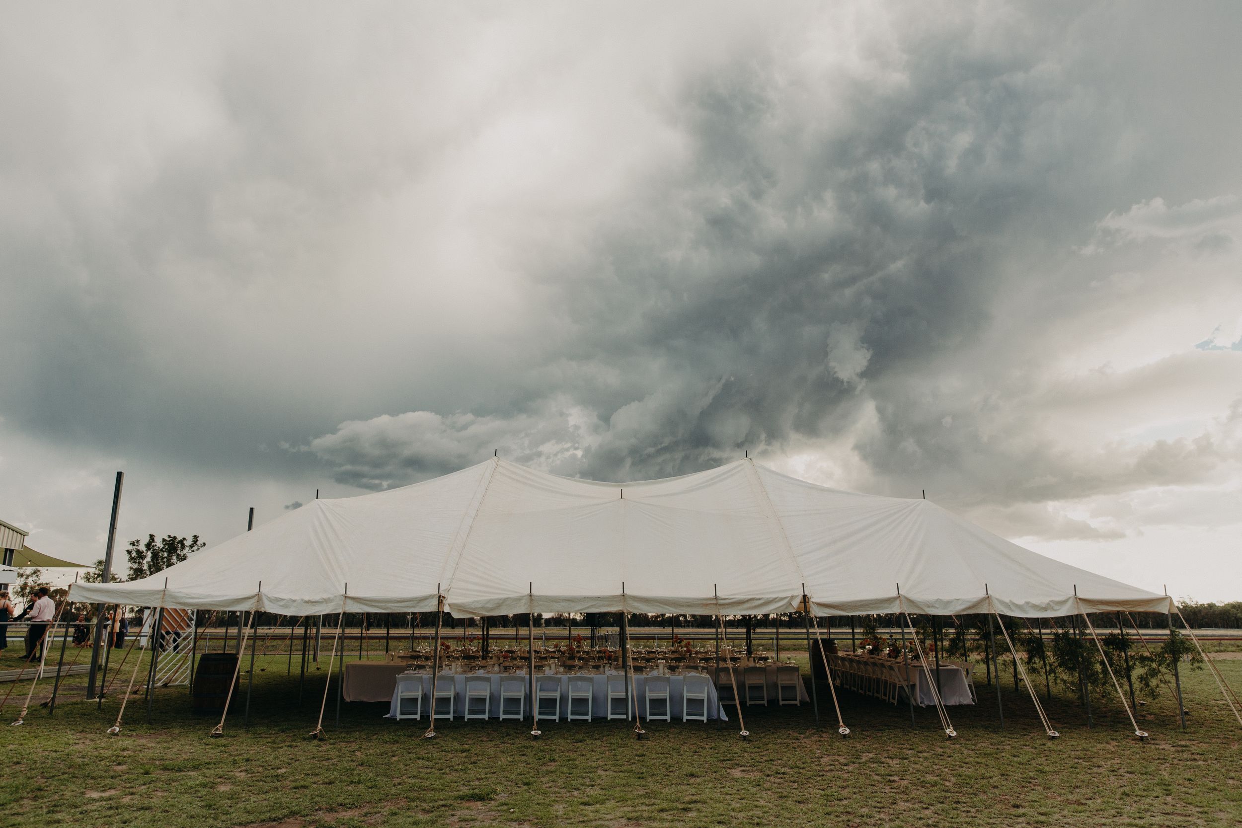 Large white wedding tent setup under dramatic cloudy sky.