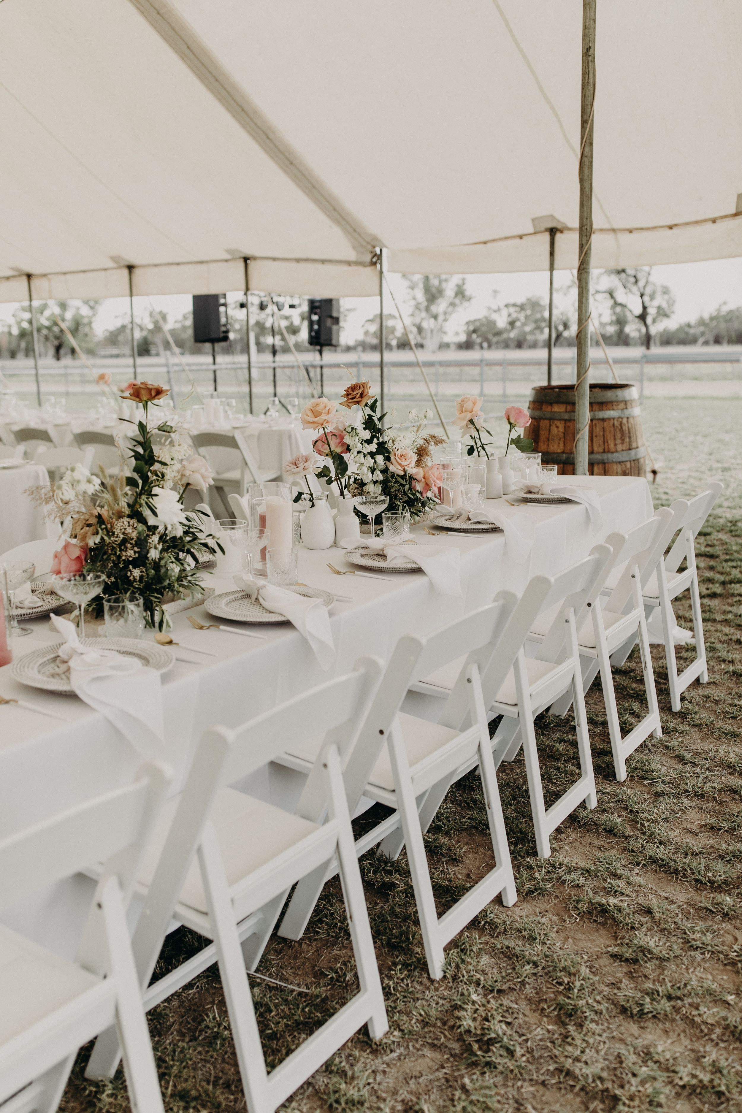 White wedding reception tables with floral centerpieces under tent canopy.