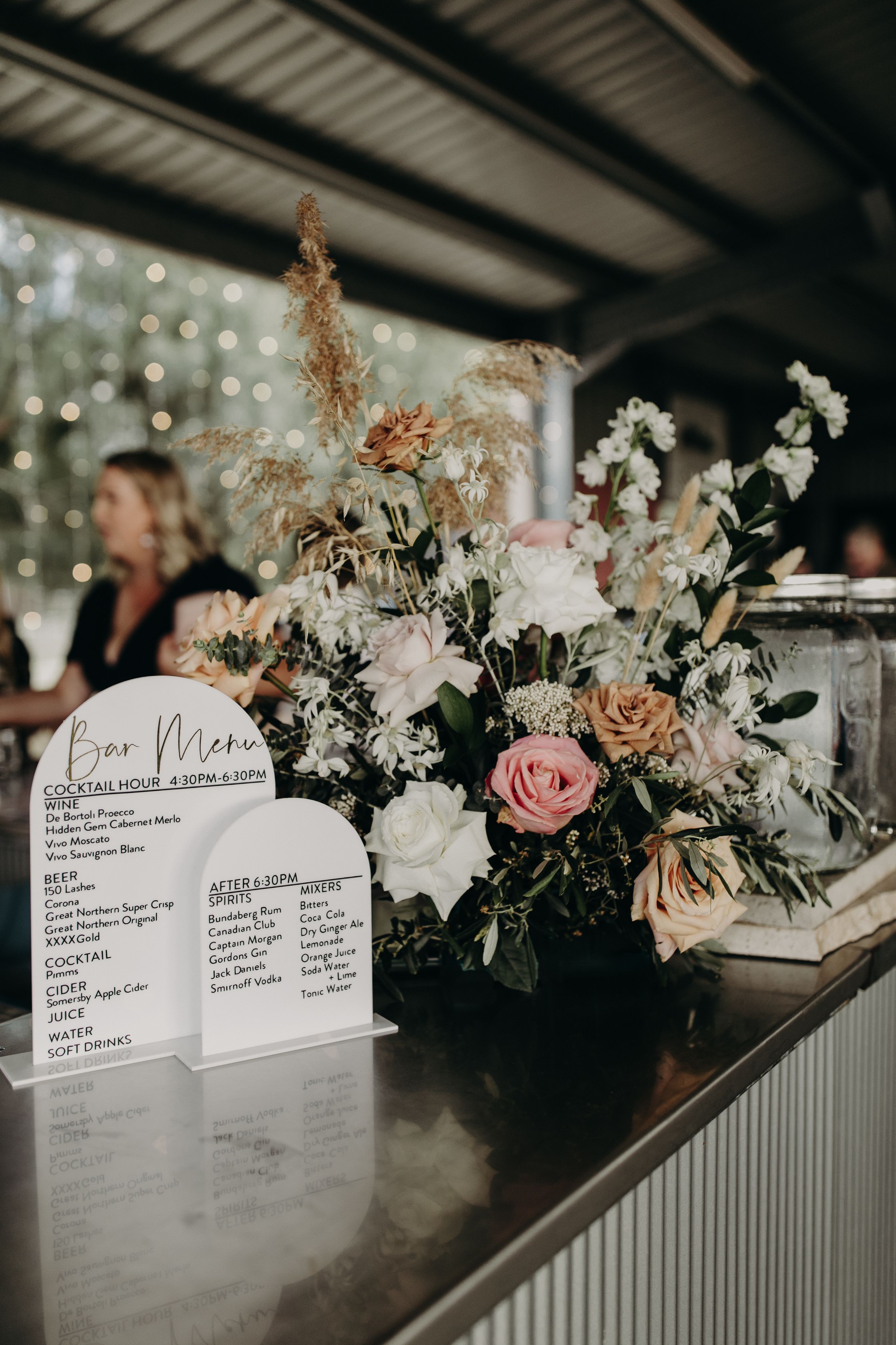 Wedding reception seating cards displayed alongside pink and white floral arrangements on metallic surface.