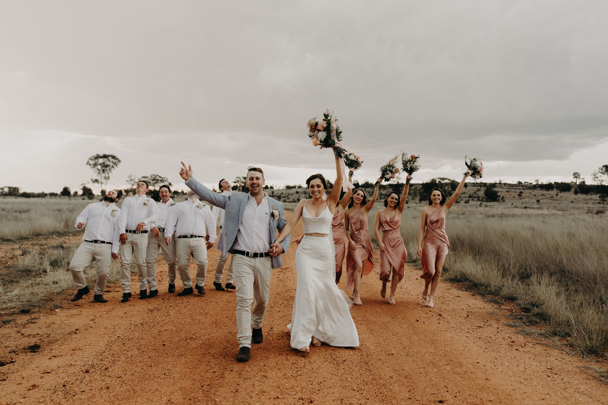 Wedding party spread out along dirt path with desert landscape in background.