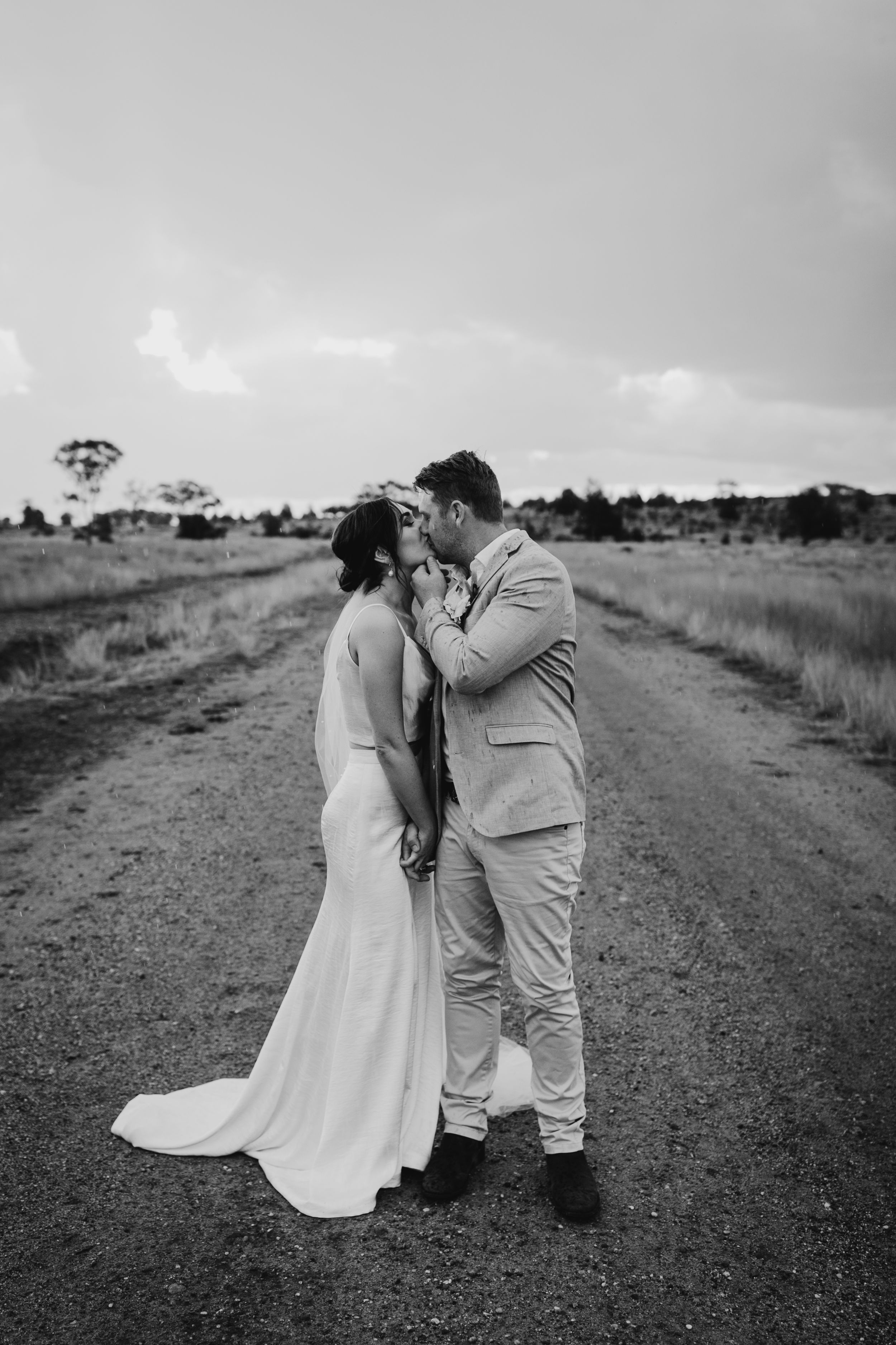 Dramatic black and white capture of newlyweds embracing on a rural road.