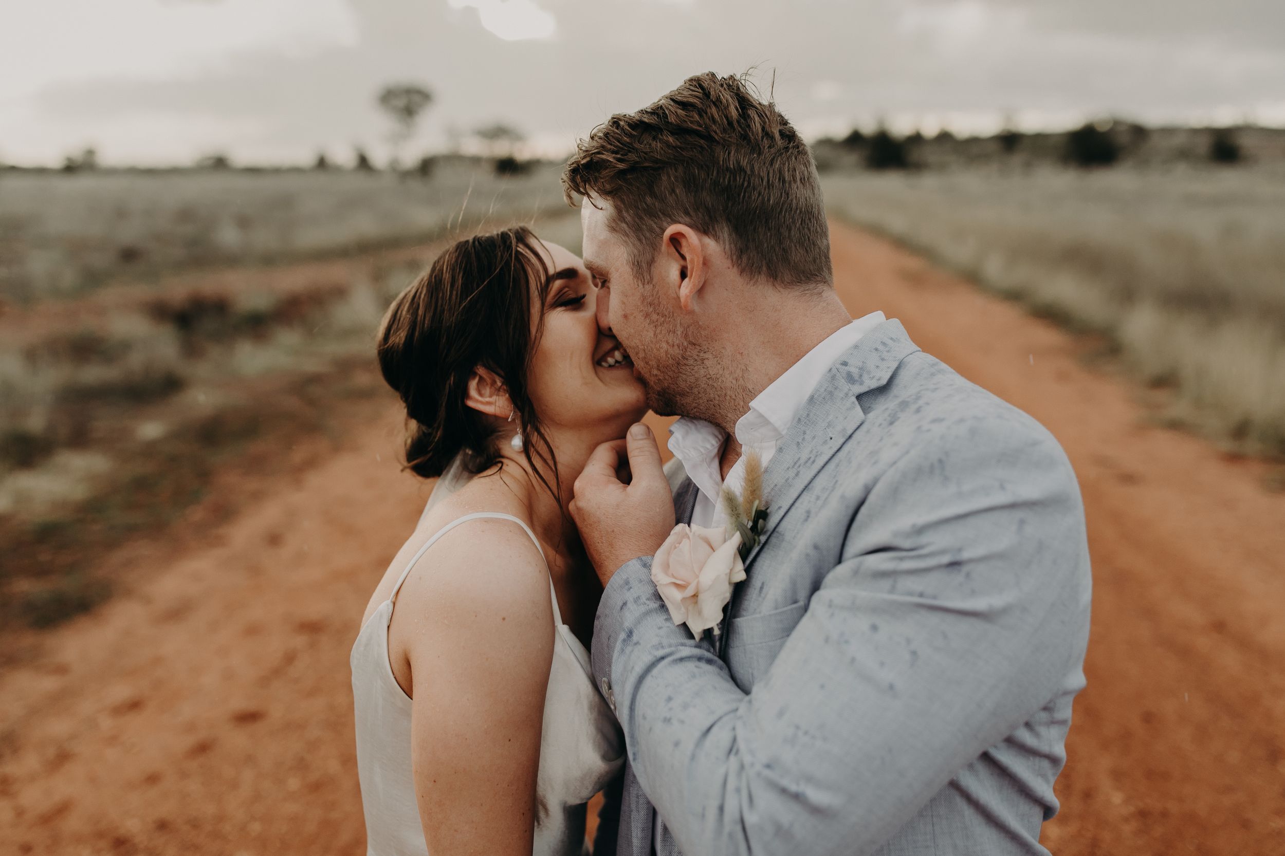 A romantic moment captured on a red dirt road with moody storm clouds overhead.