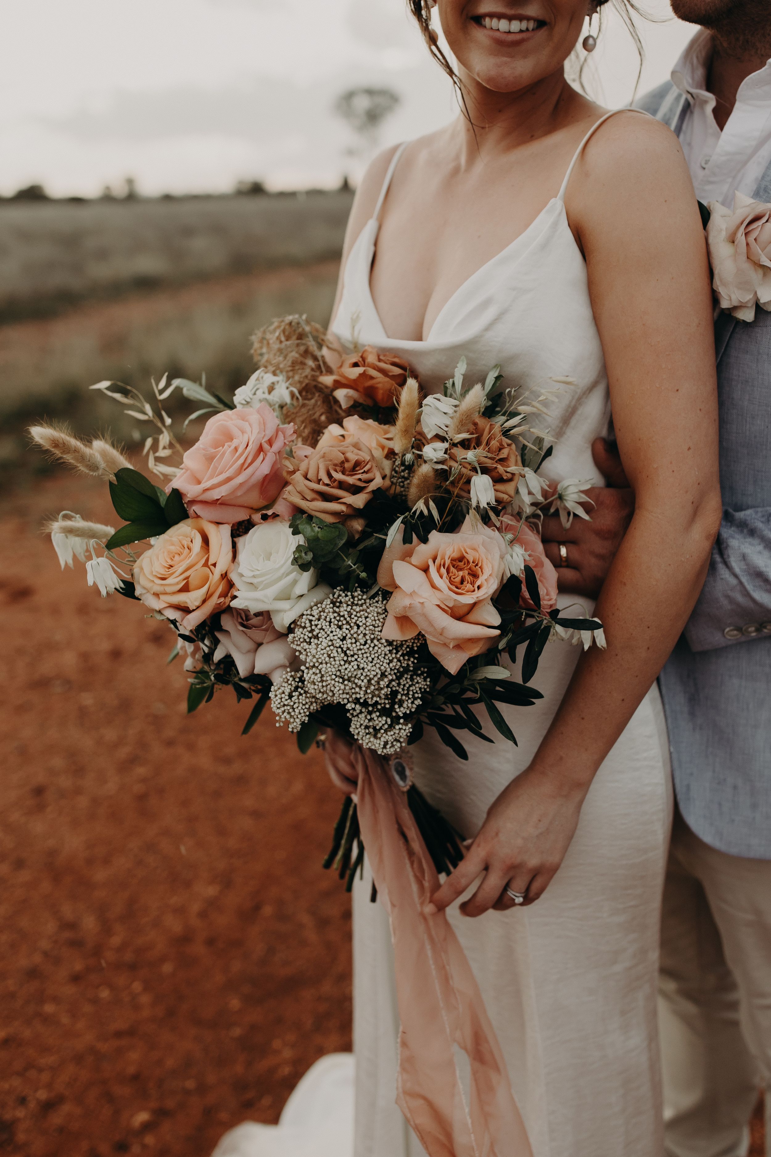 A stunning bridal bouquet with peach roses and white flowers against red earth background.