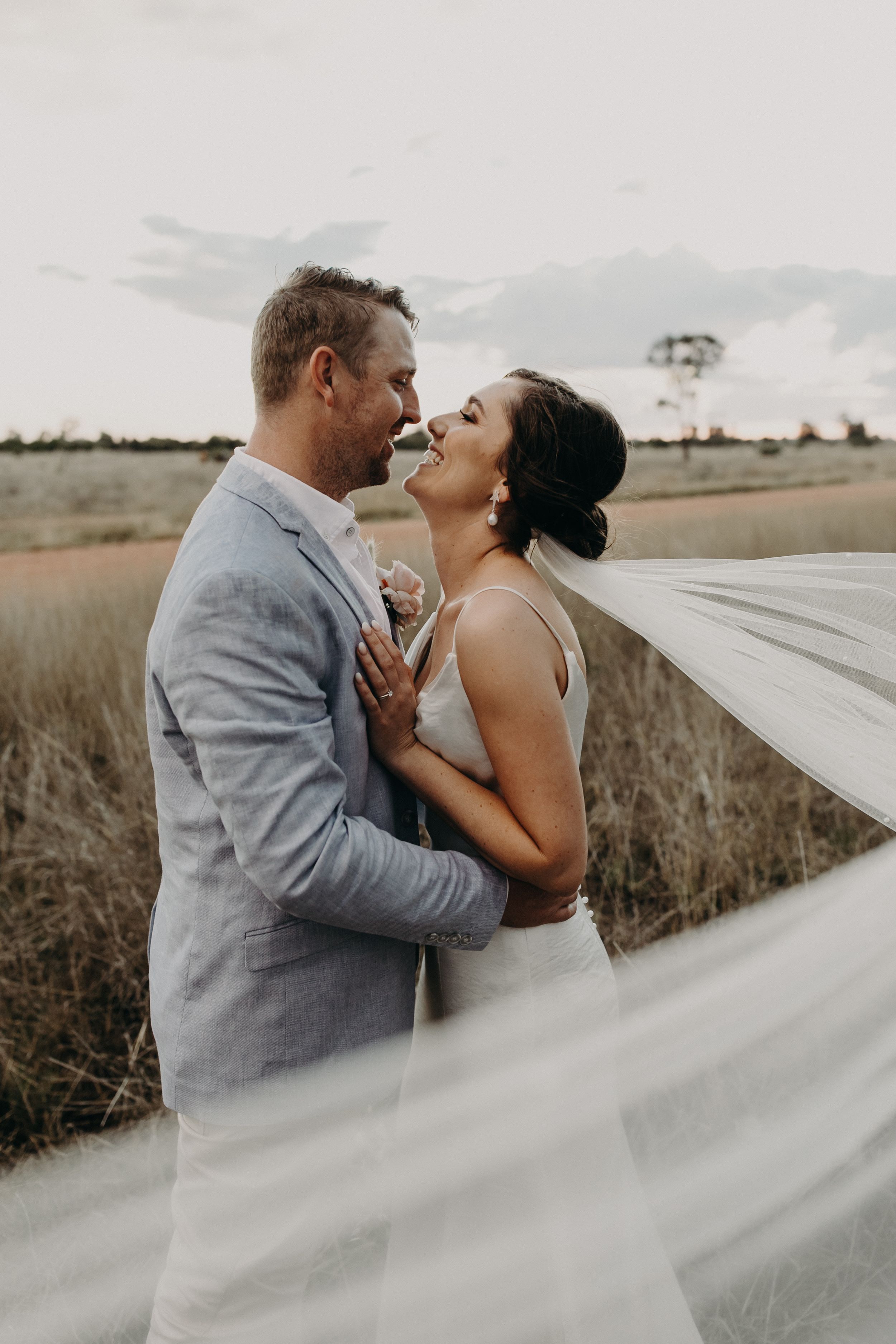 A romantic moment with flowing veil captured against an outback landscape.