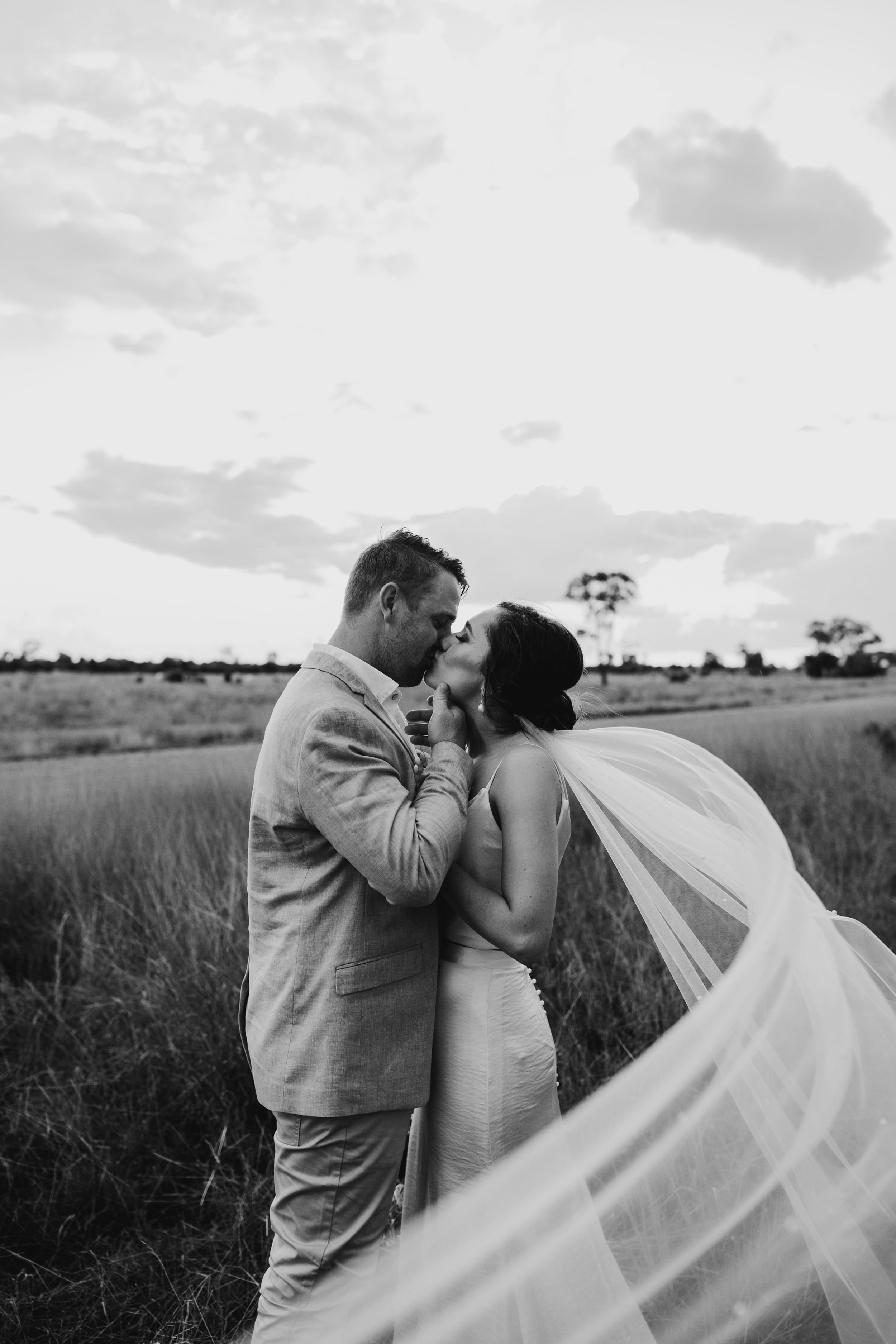A romantic black and white wedding photo with a flowing veil in a rustic outdoor setting.