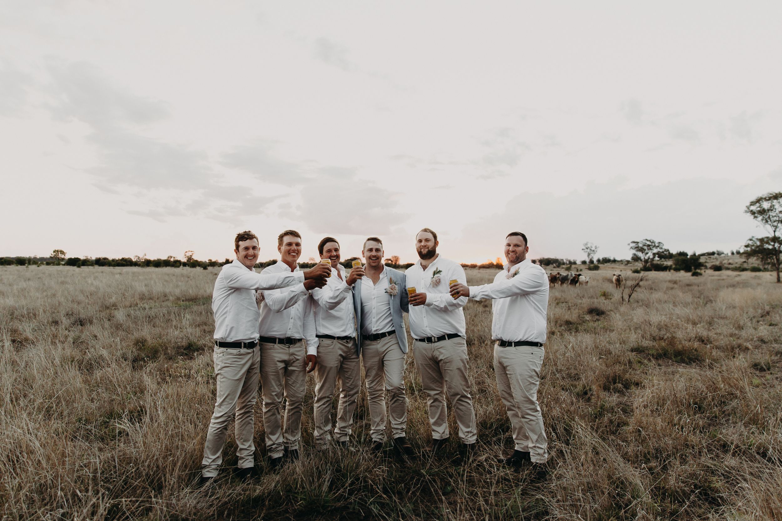 Groomsmen in light colored suits pose together in an open field.