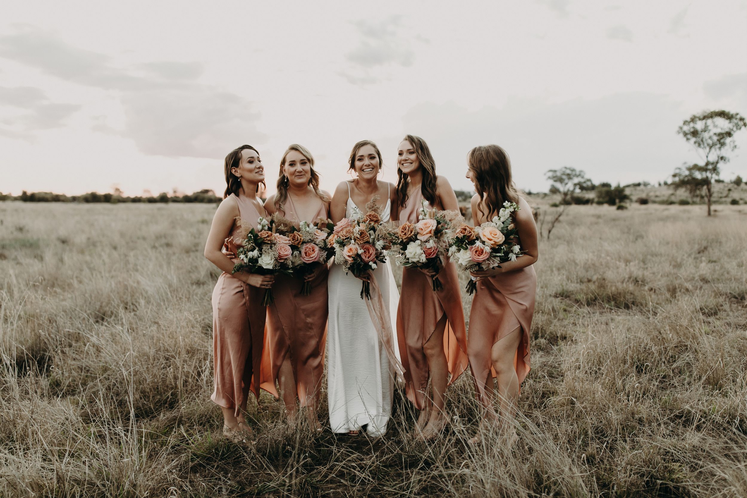 Wedding party poses together in an open field during sunset.