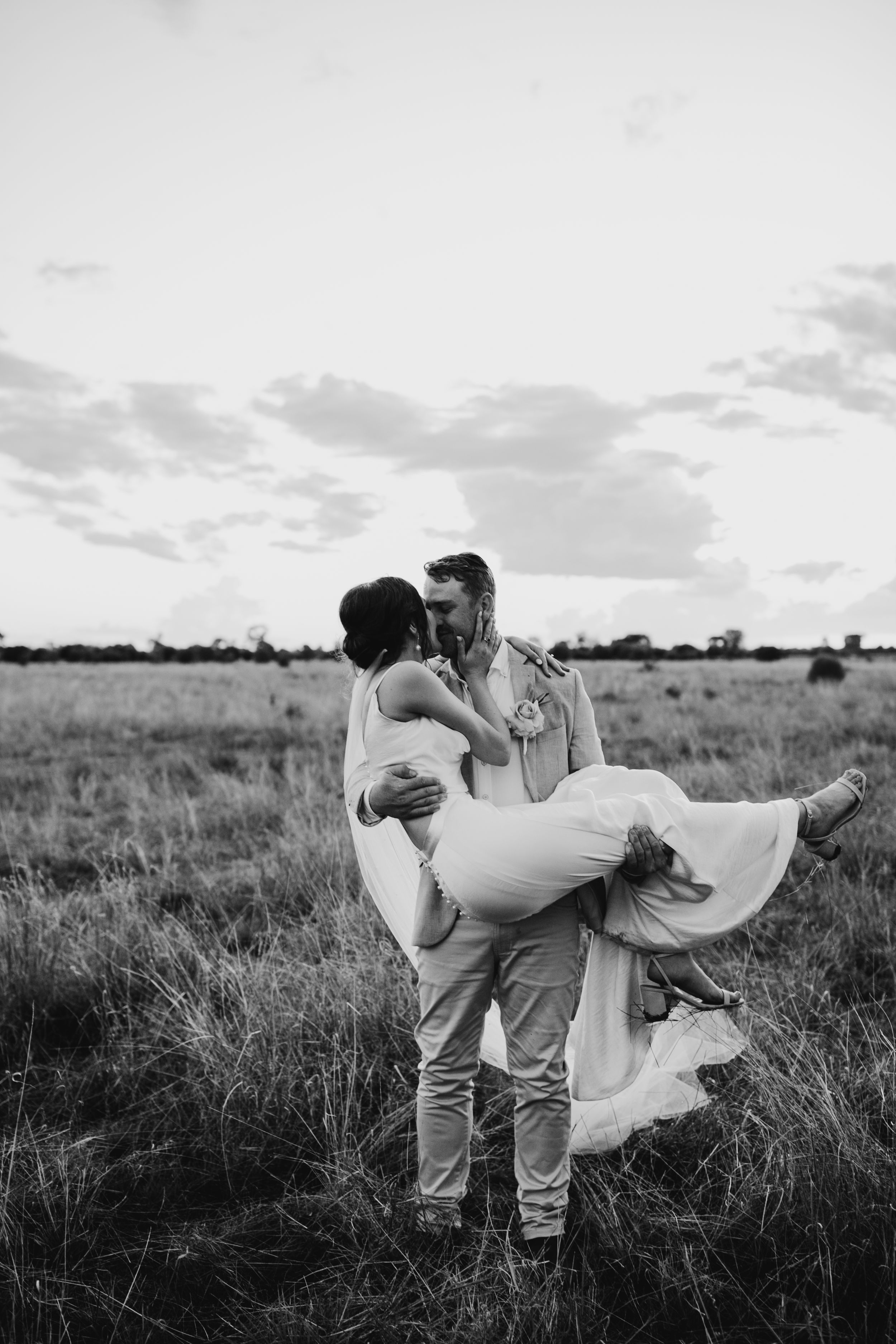 A romantic black and white photo of a couple embracing in a field at sunset with flowing dress.
