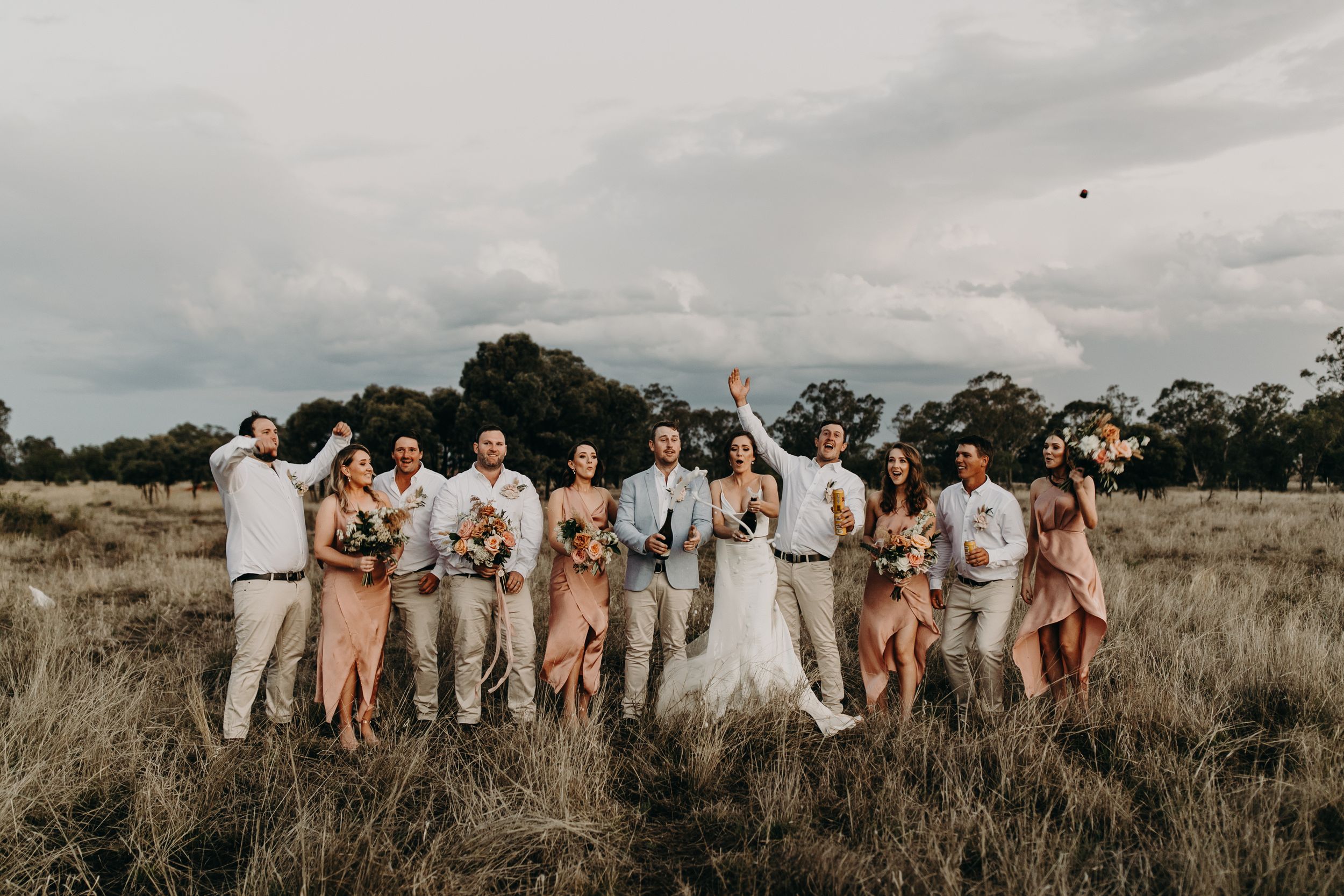 Wedding party celebrates in an open field wearing neutral colors and formal attire.
