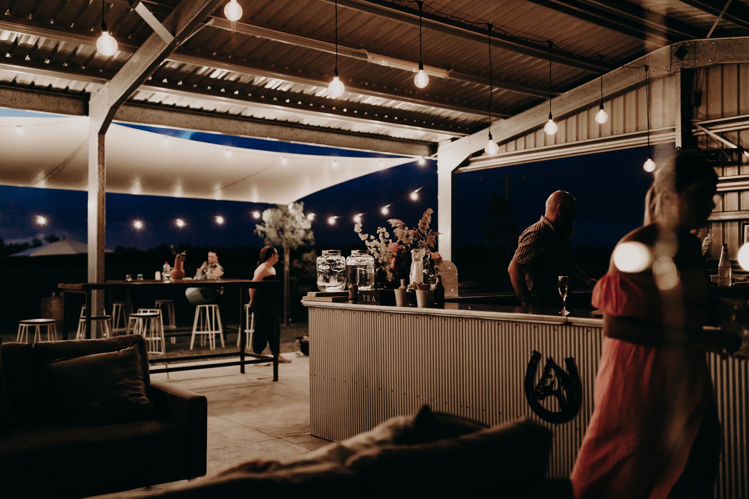 Evening reception venue with string lights and rustic bar setup.