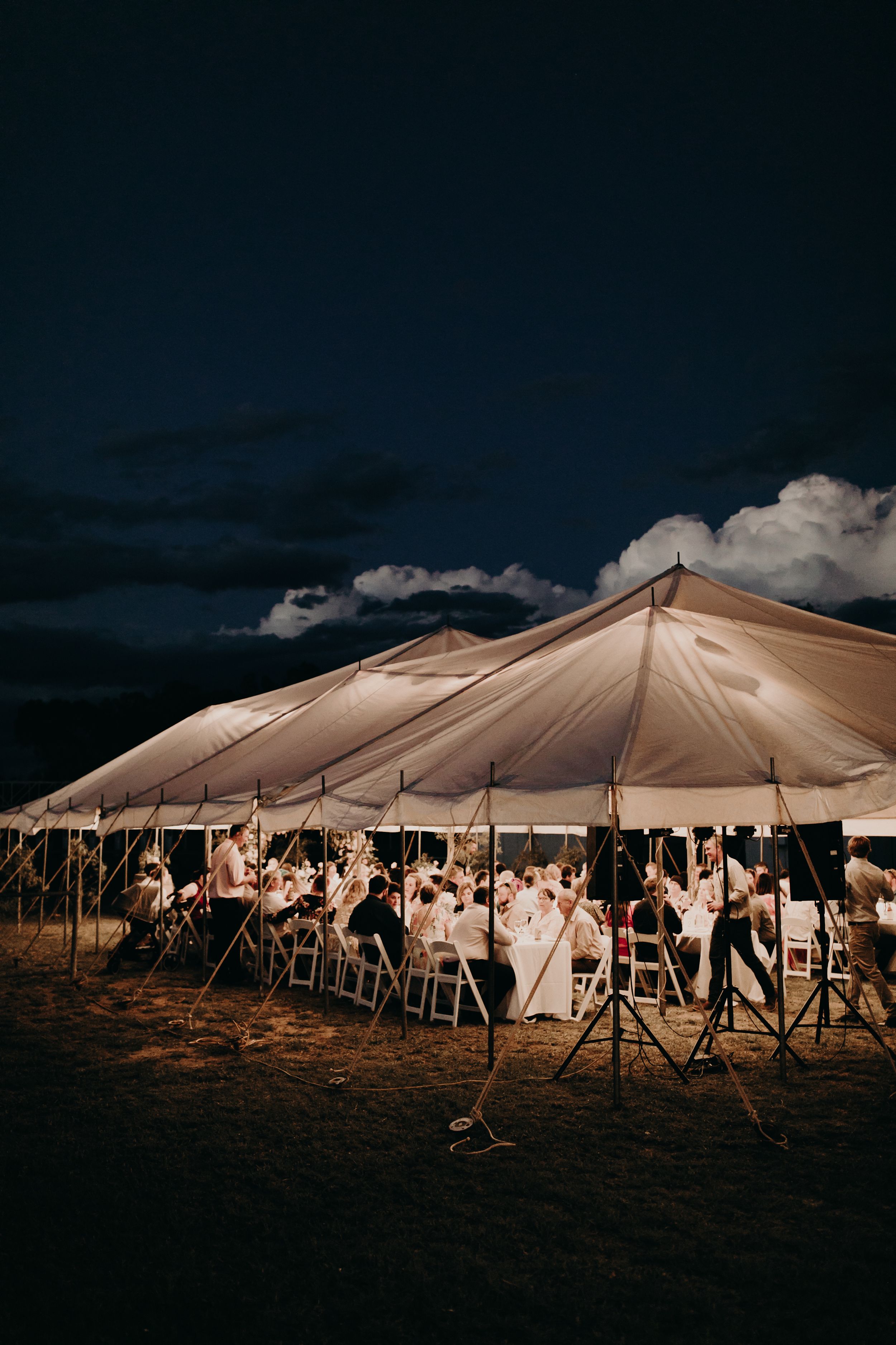 Large white wedding tent glows from within against a dramatic evening sky.