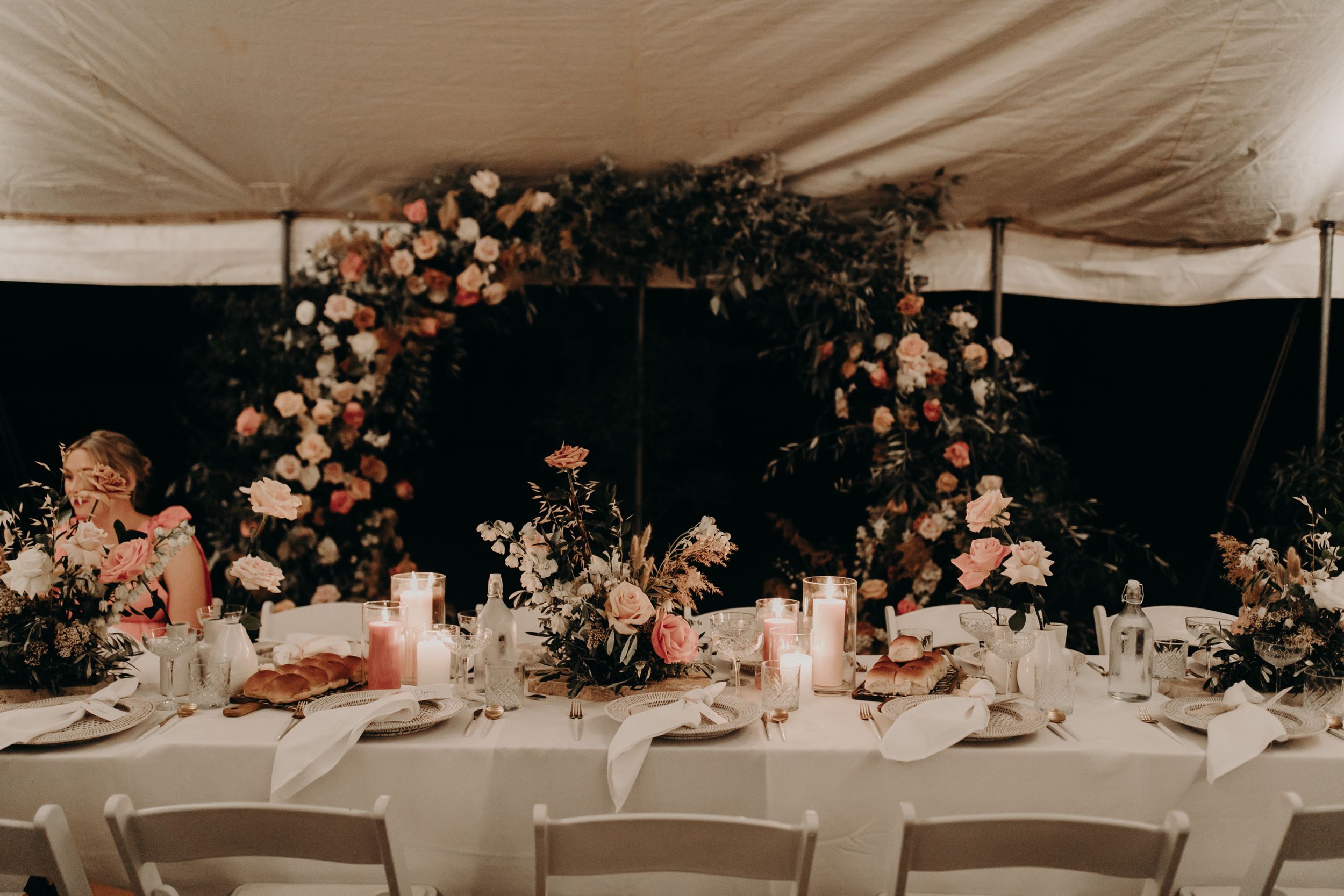 Elegant wedding reception tables set with floral arrangements under a white tent.