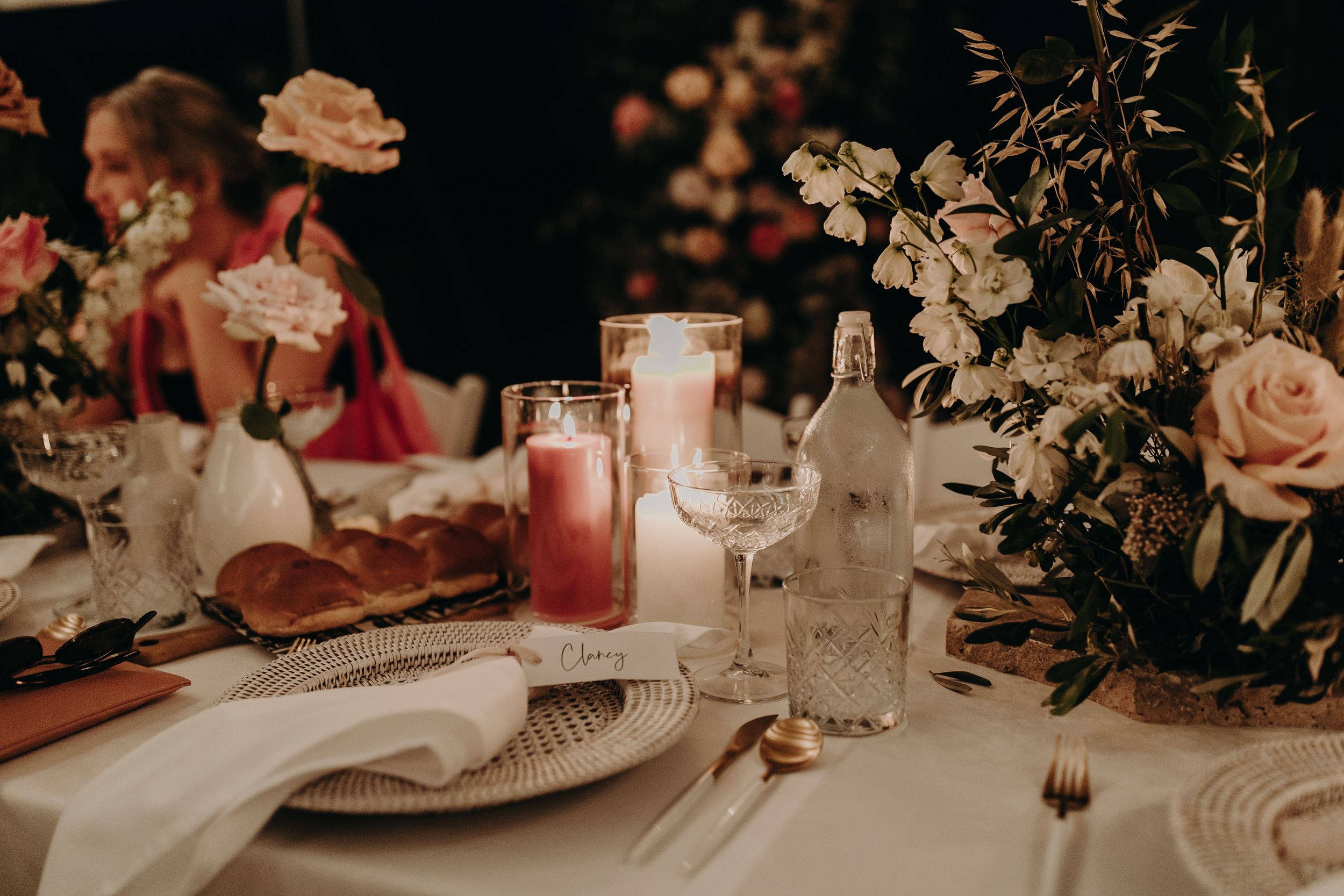 Romantic table setting with pink roses, candles and elegant place settings at evening reception.