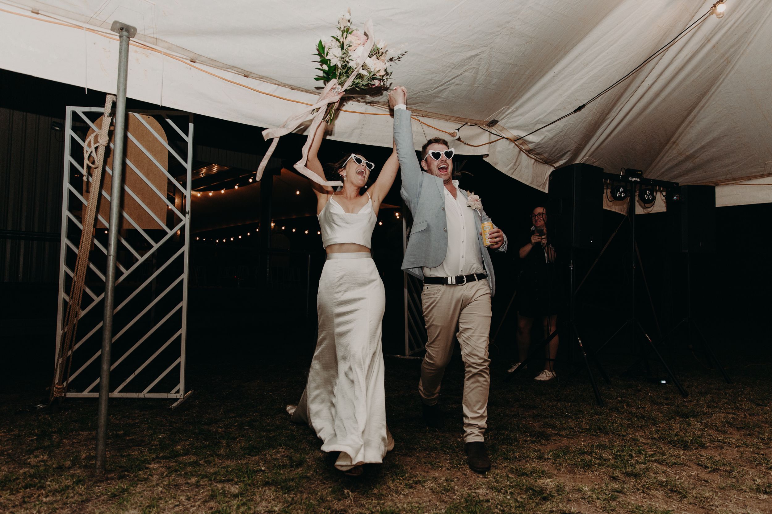 Guests dancing and celebrating at an outdoor wedding reception under a white tent.