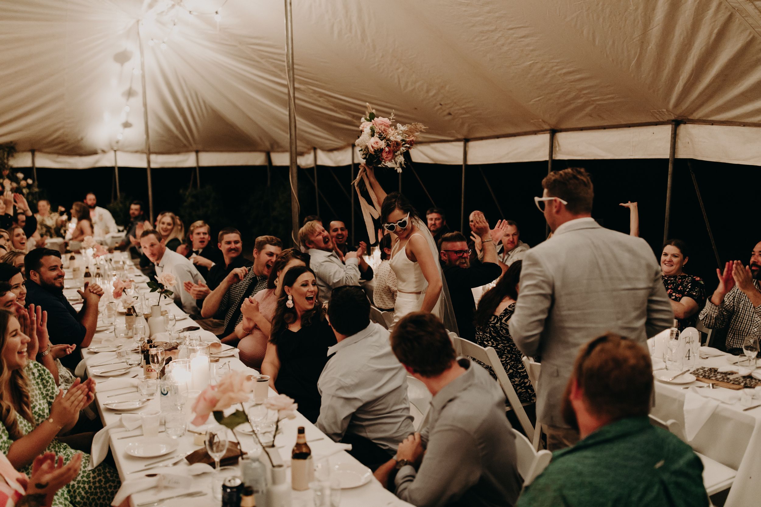 Wedding reception dinner under a tent with guests celebrating at long tables.