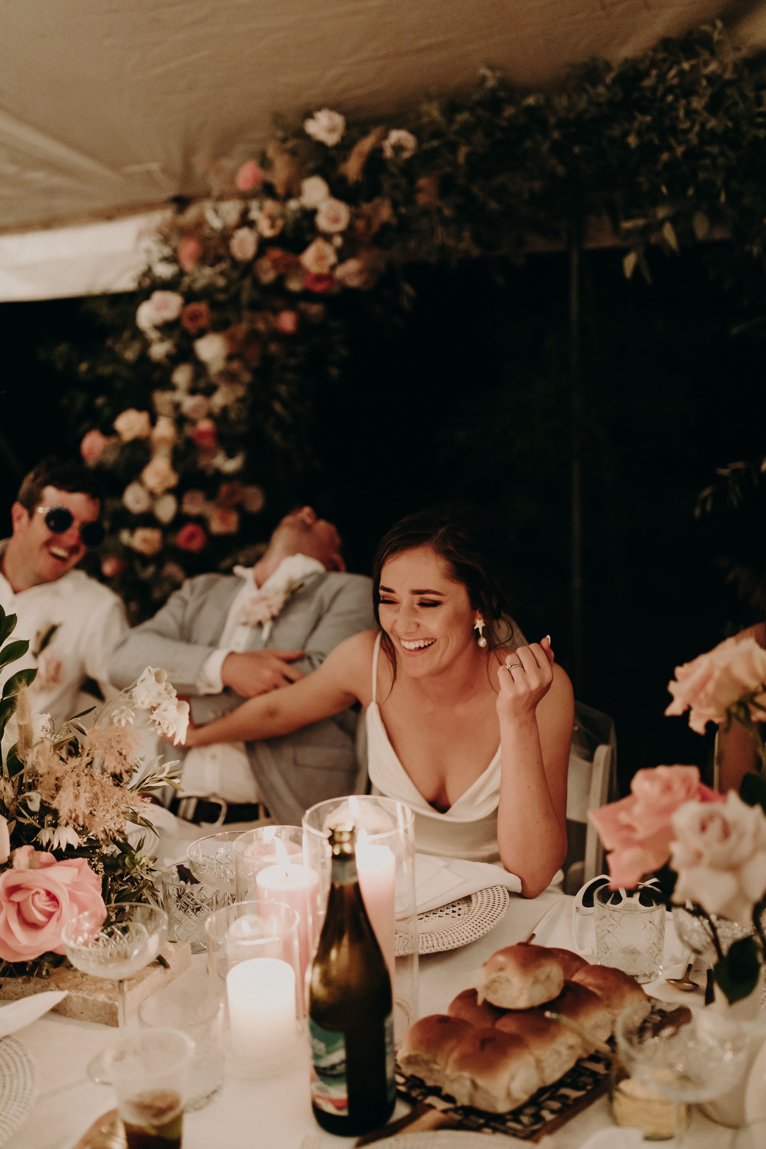 Candlelit wedding reception table with floral centerpieces and guests enjoying dinner.