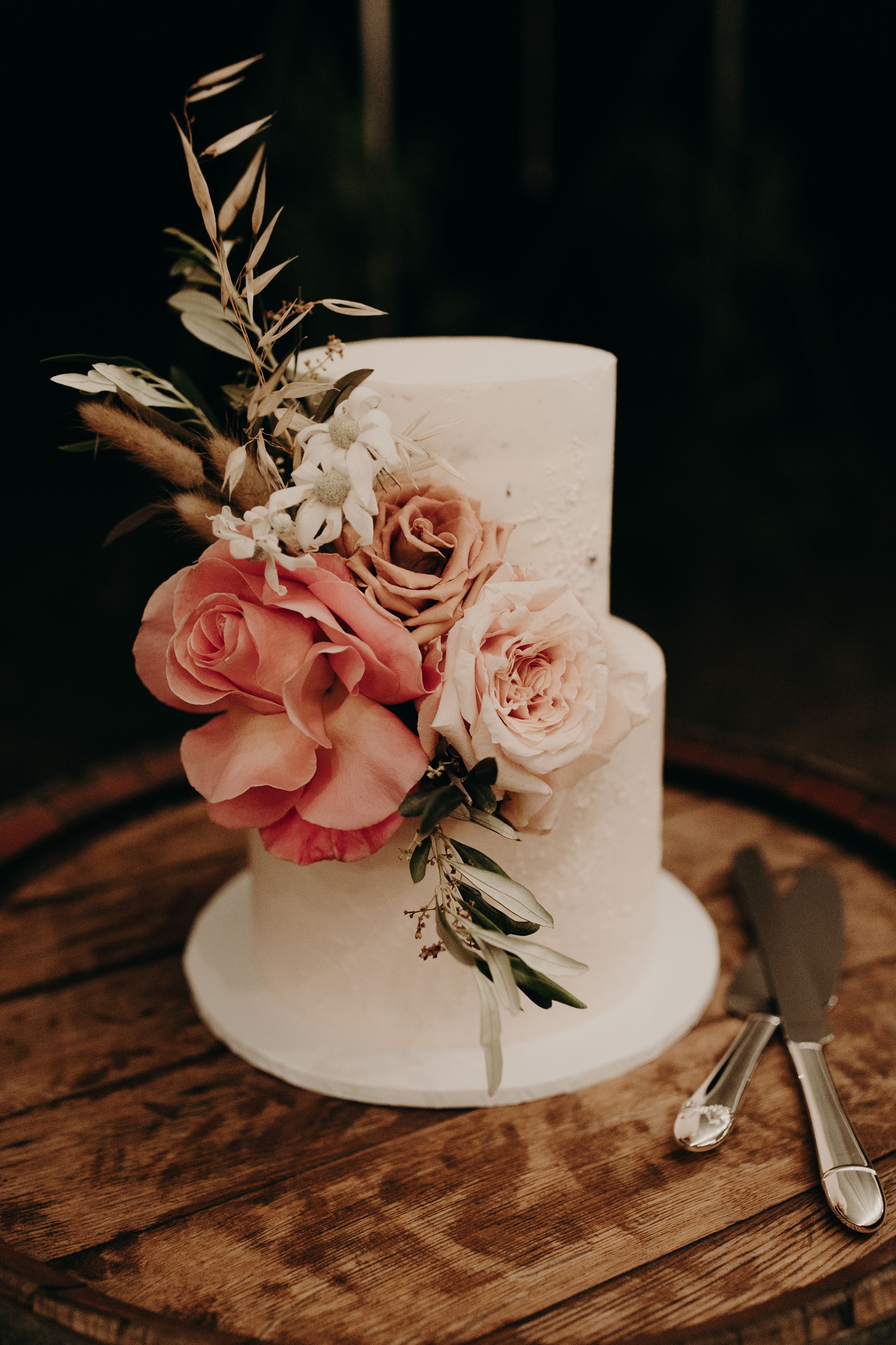 Simple white wedding cake decorated with pink roses and greenery on a rustic wooden table.