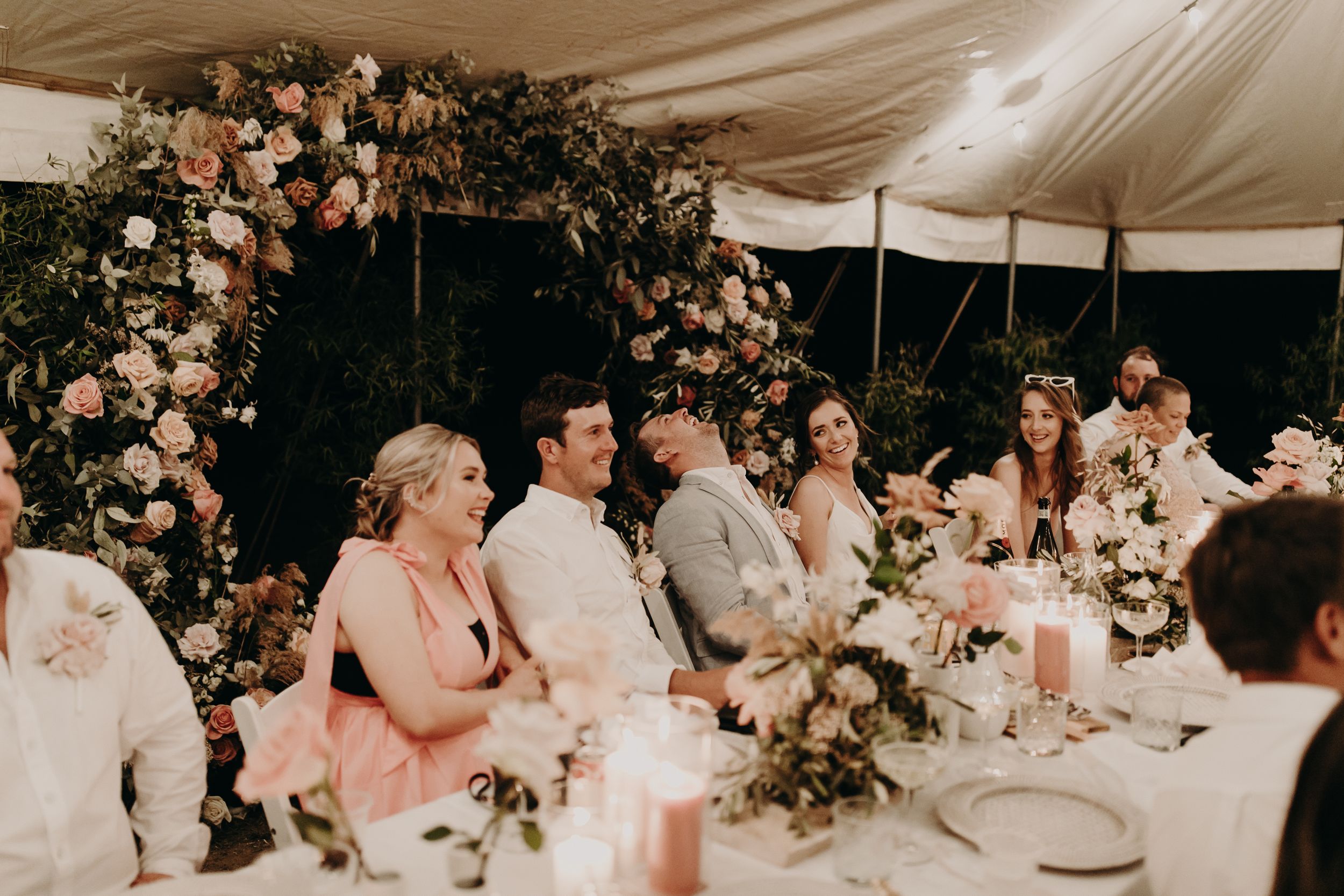 Wedding reception tables decorated with pink floral arrangements under a white tent.