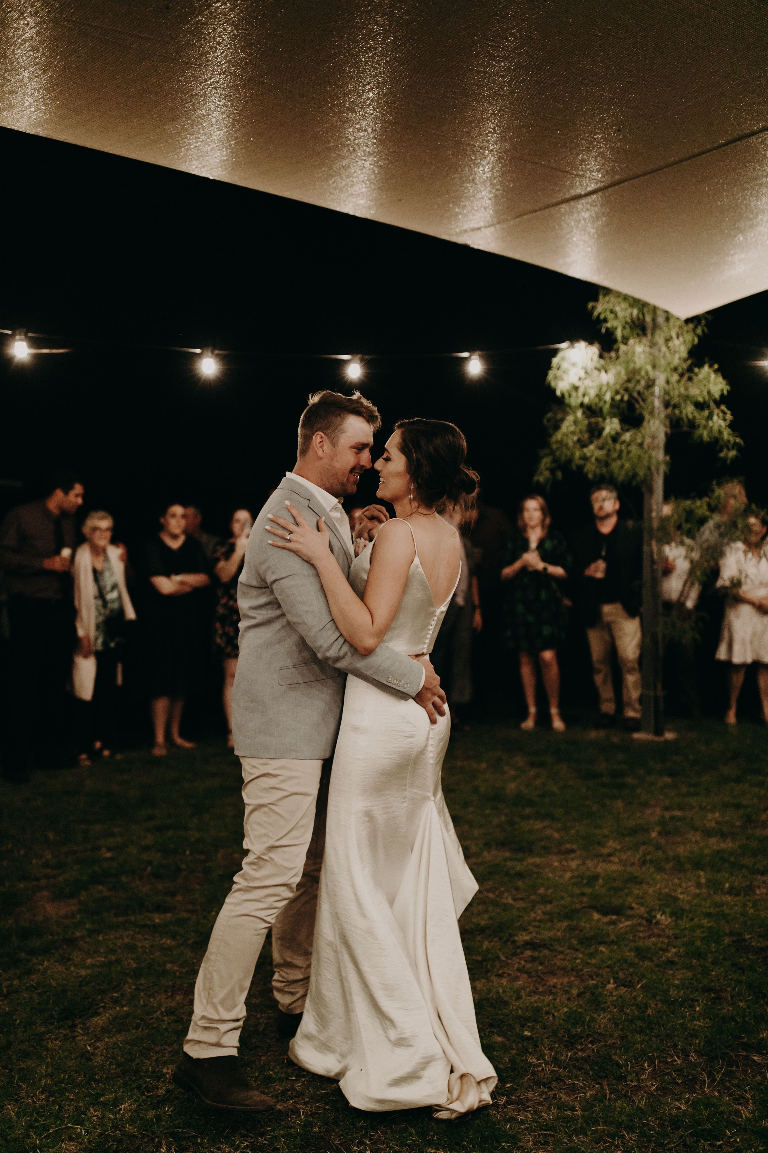 Couple shares their first dance under string lights at an outdoor evening wedding reception.