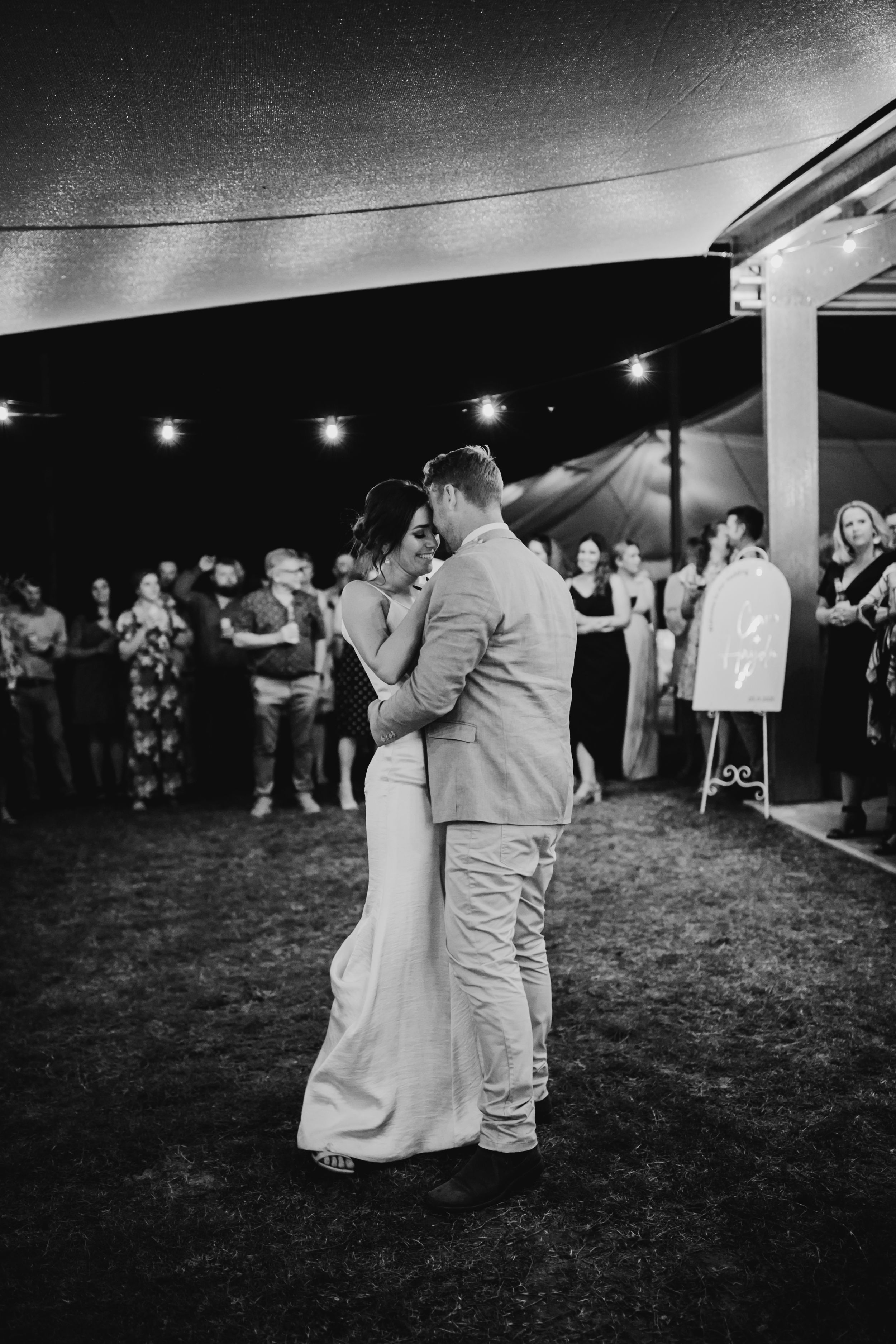 Wedding party dances together during an evening outdoor reception under string lights.