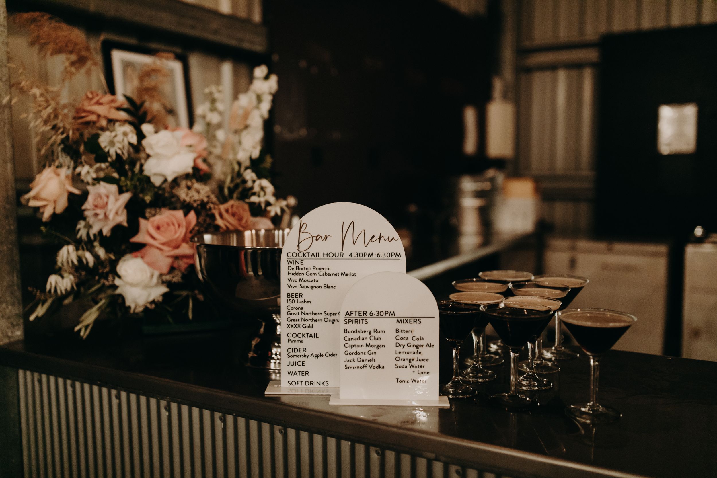 Wedding reception details with floral arrangements and signage on dark wooden tables.