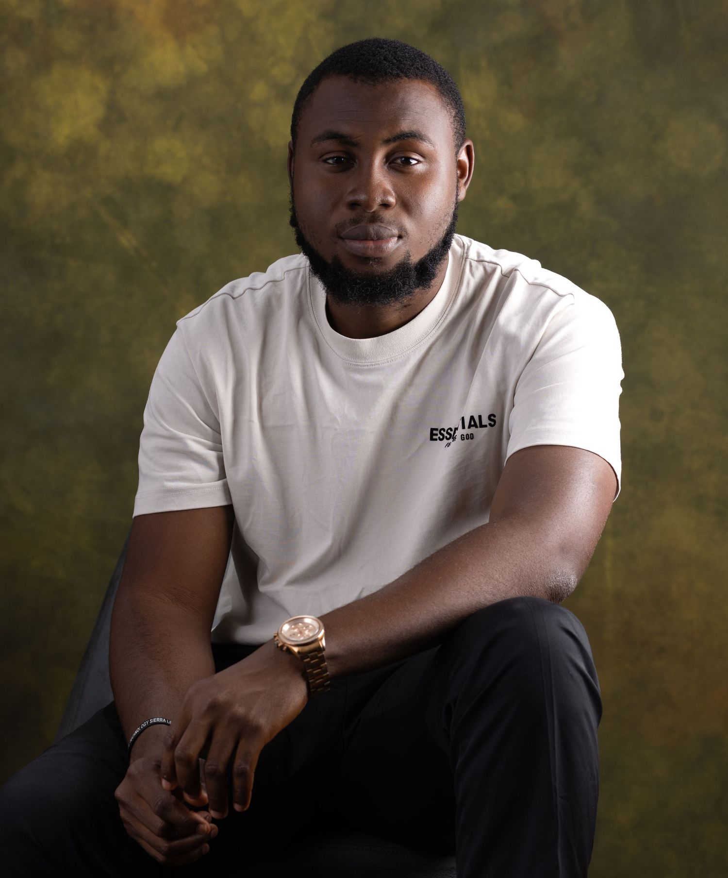 Portrait of a person in a white t-shirt seated against a textured brown backdrop.