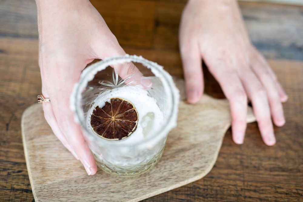 Hands placing a dark round object in a glass container on a wooden surface.