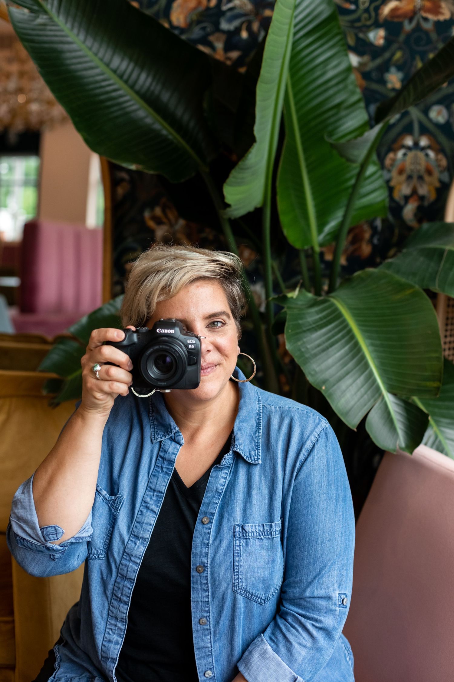 Aly Darin sitting on chair near plants. Camera in hand. Senior photographer