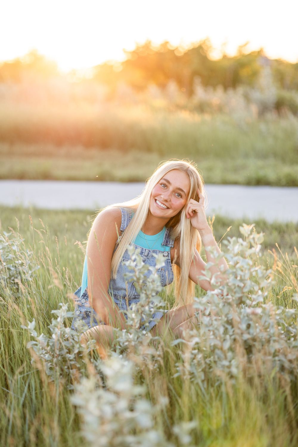 Person in denim overalls sitting in tall grass during golden hour.
